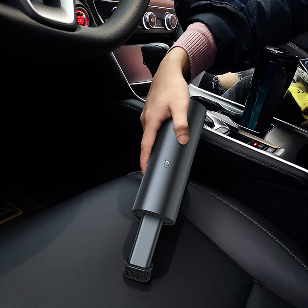Eine Hand greift in ein Auto und hält einen schwarzen Handstaubsauger über einen Autositz.