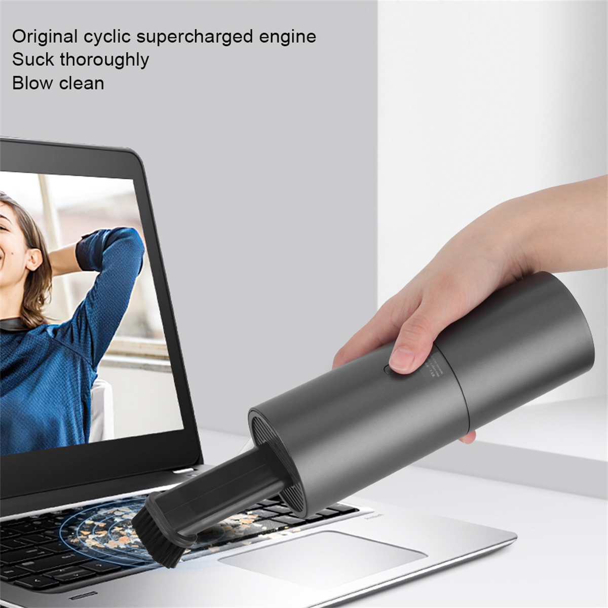 Person saugt einen Laptop mit einem kleinen Handstaubsauger ab.