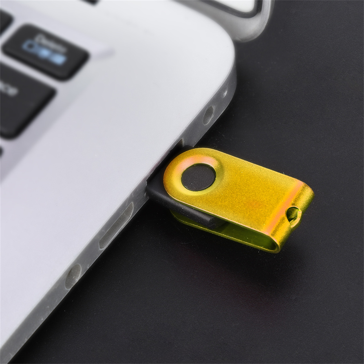 Ein goldener USB-Stick, der in einen silbernen Laptop gesteckt ist, auf dunklem Hintergrund.