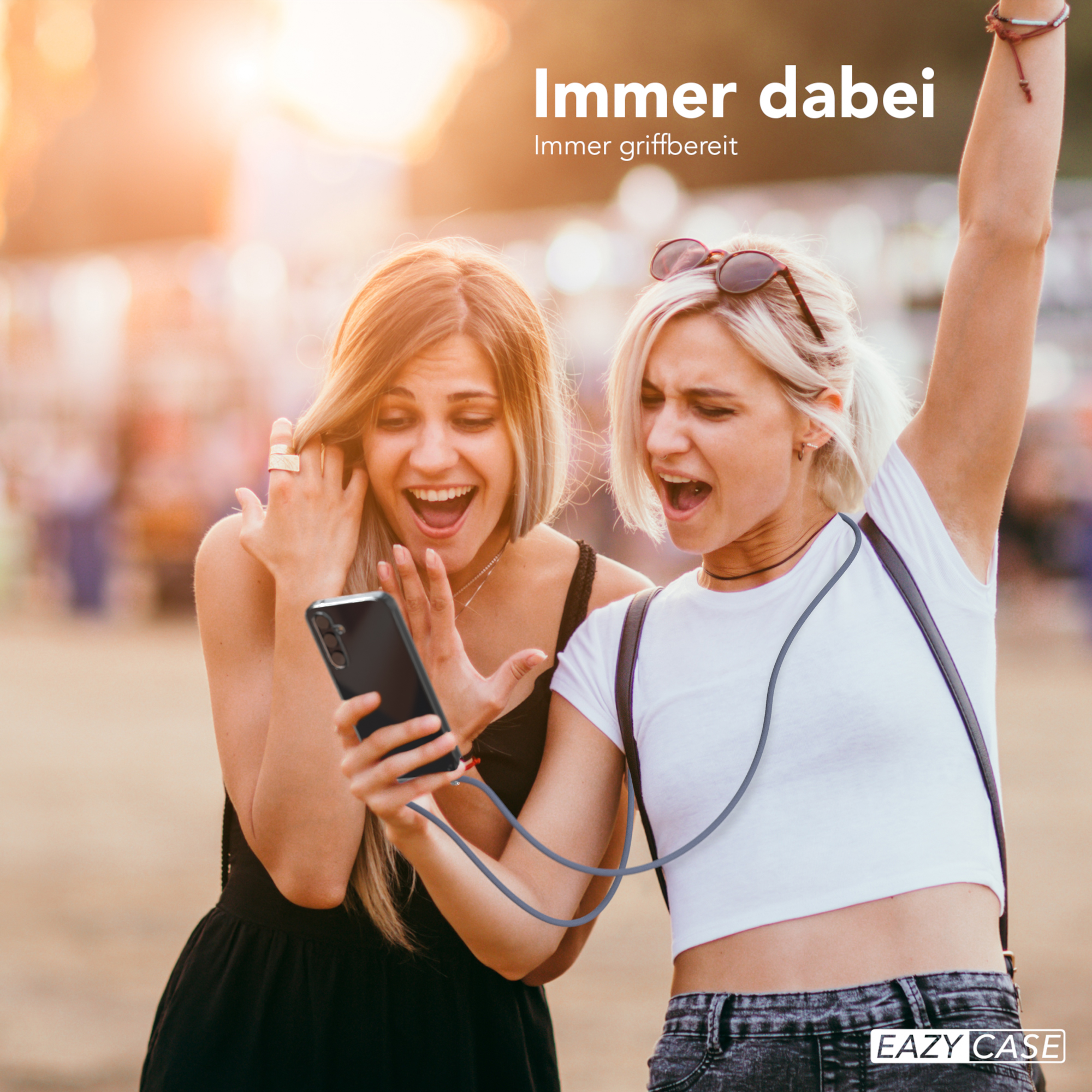 Zwei aufgeregte Frauen halten ein Telefon mit einem Lanyard, mit unscharfem Hintergrund.