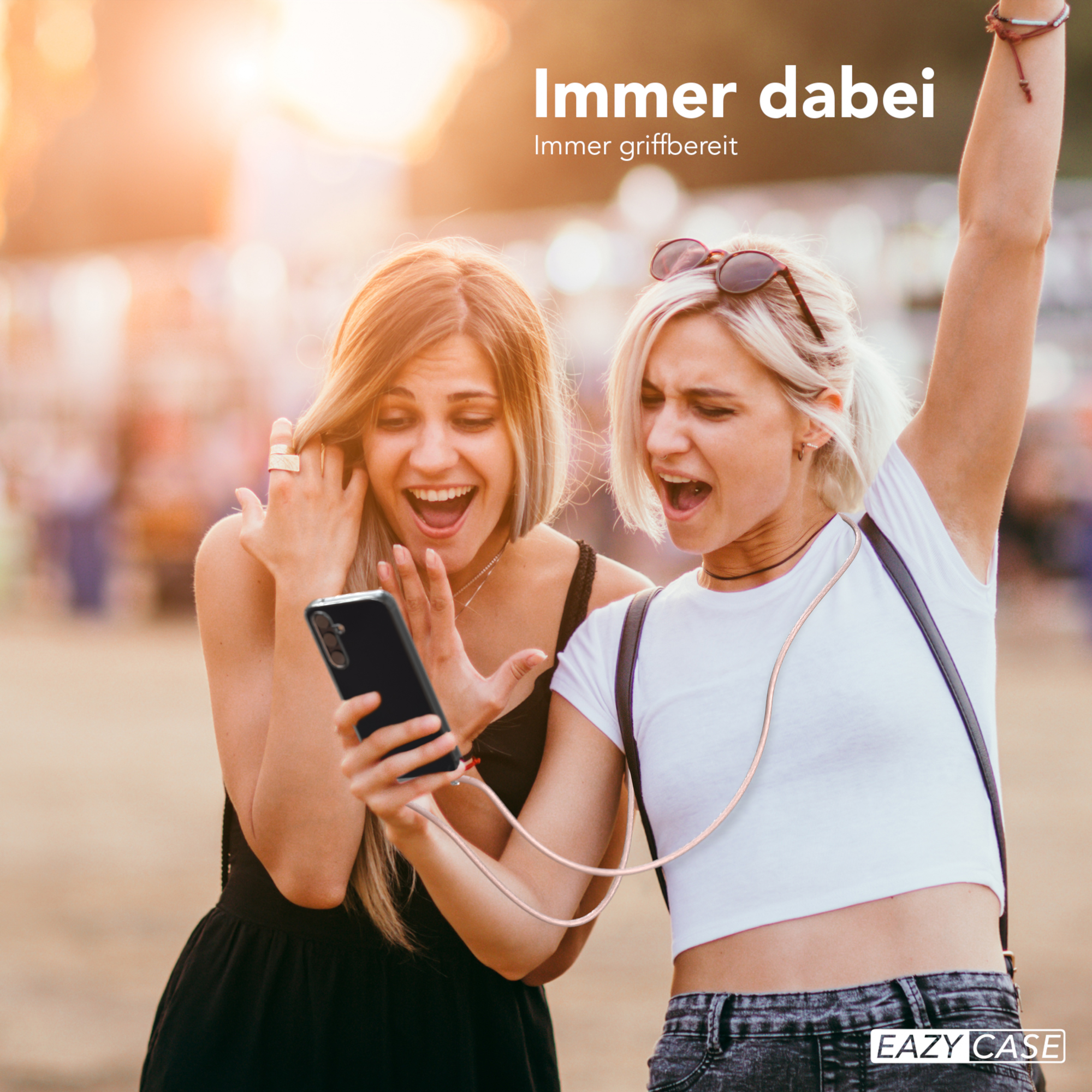 Zwei Frauen schauen auf ein Telefon. Eine hält es und lächelt, mit einer goldenen Kette.