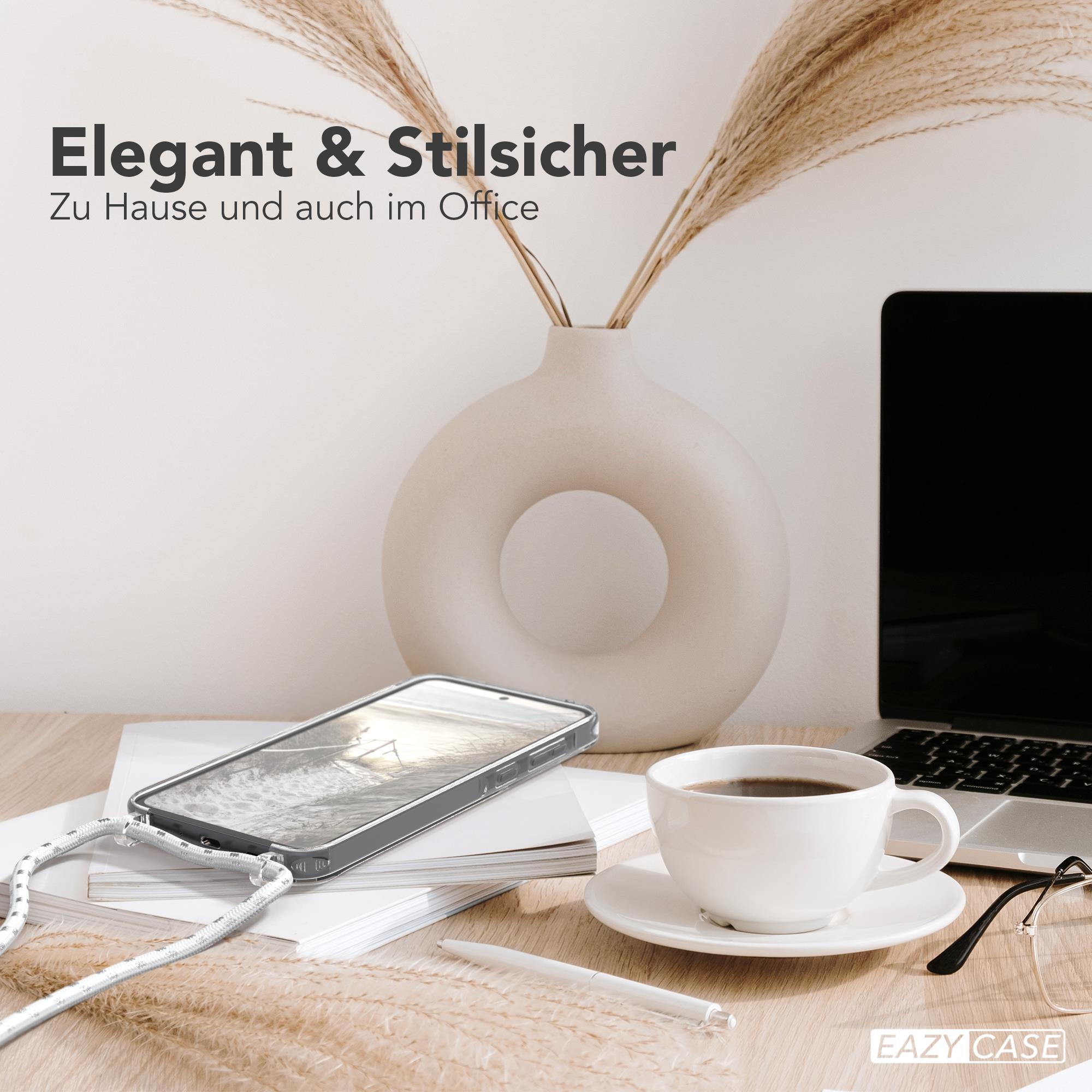 Telefon mit Riemen vor Laptop, Kaffeetasse und Brille. Neutraler Hintergrund.