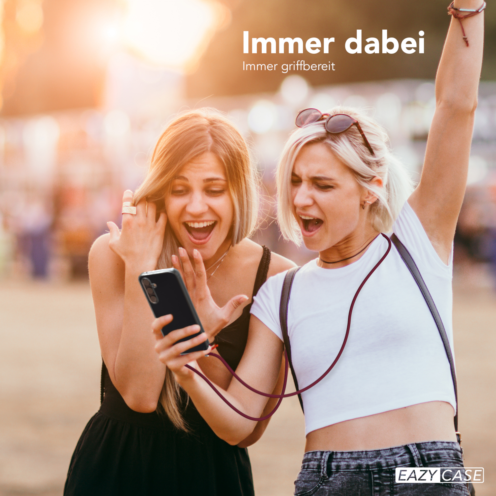 Zwei Frauen schauen auf ein Handy. Eine trägt ein weißes Hemd, die andere ein schwarzes Kleid.
