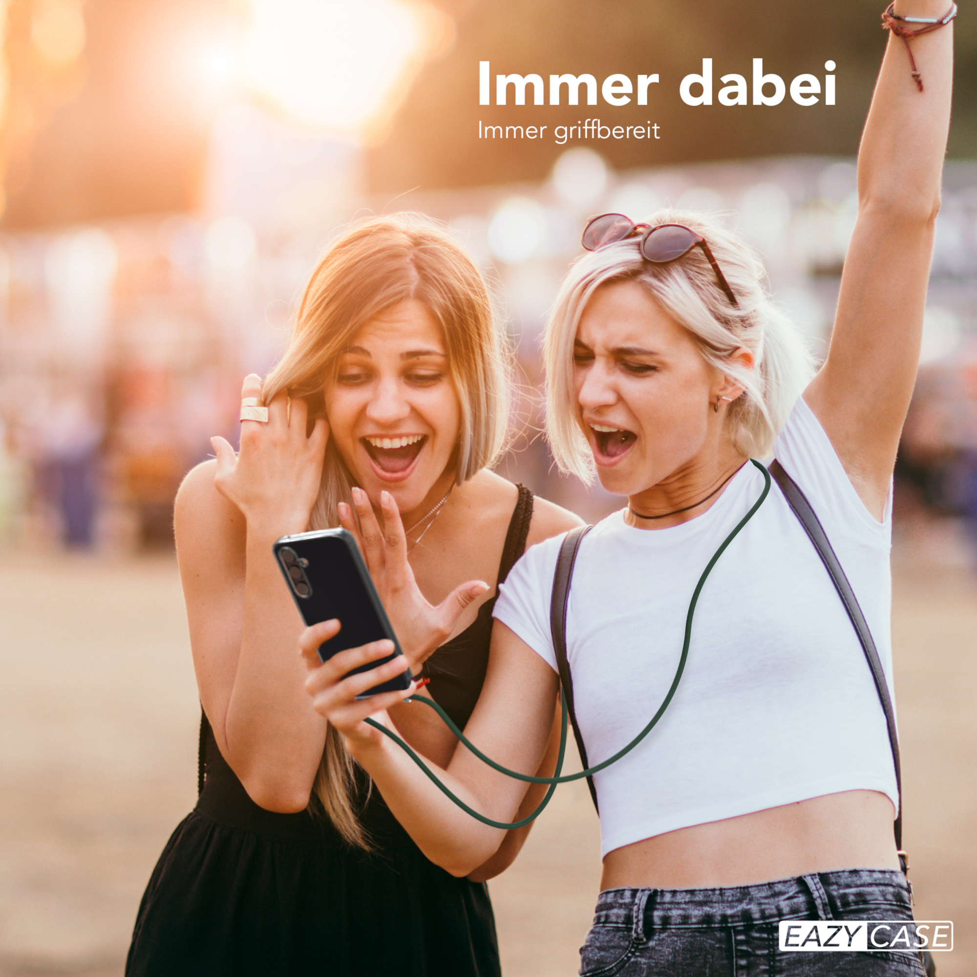 Zwei Frauen schauen auf ein Telefon. Eine hat eine Sonnenbrille auf dem Kopf, die andere ein Telefon mit Gurt.