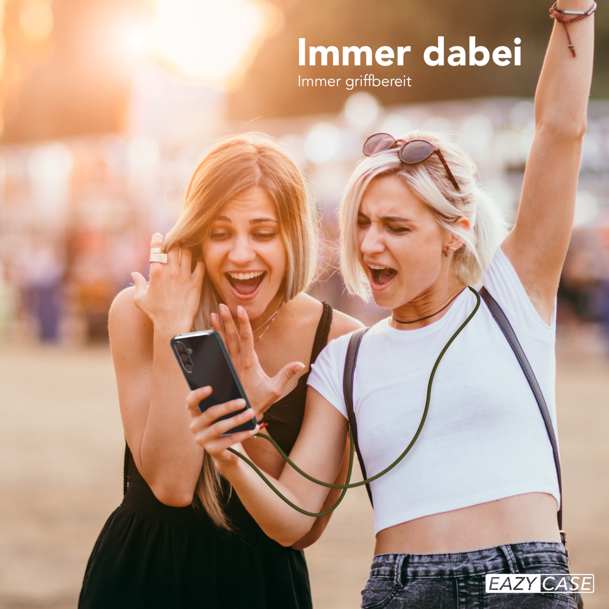 Zwei Frauen schauen im Freien auf ein Telefon. Eine hat den Arm gehoben. Text: Immer dabei.