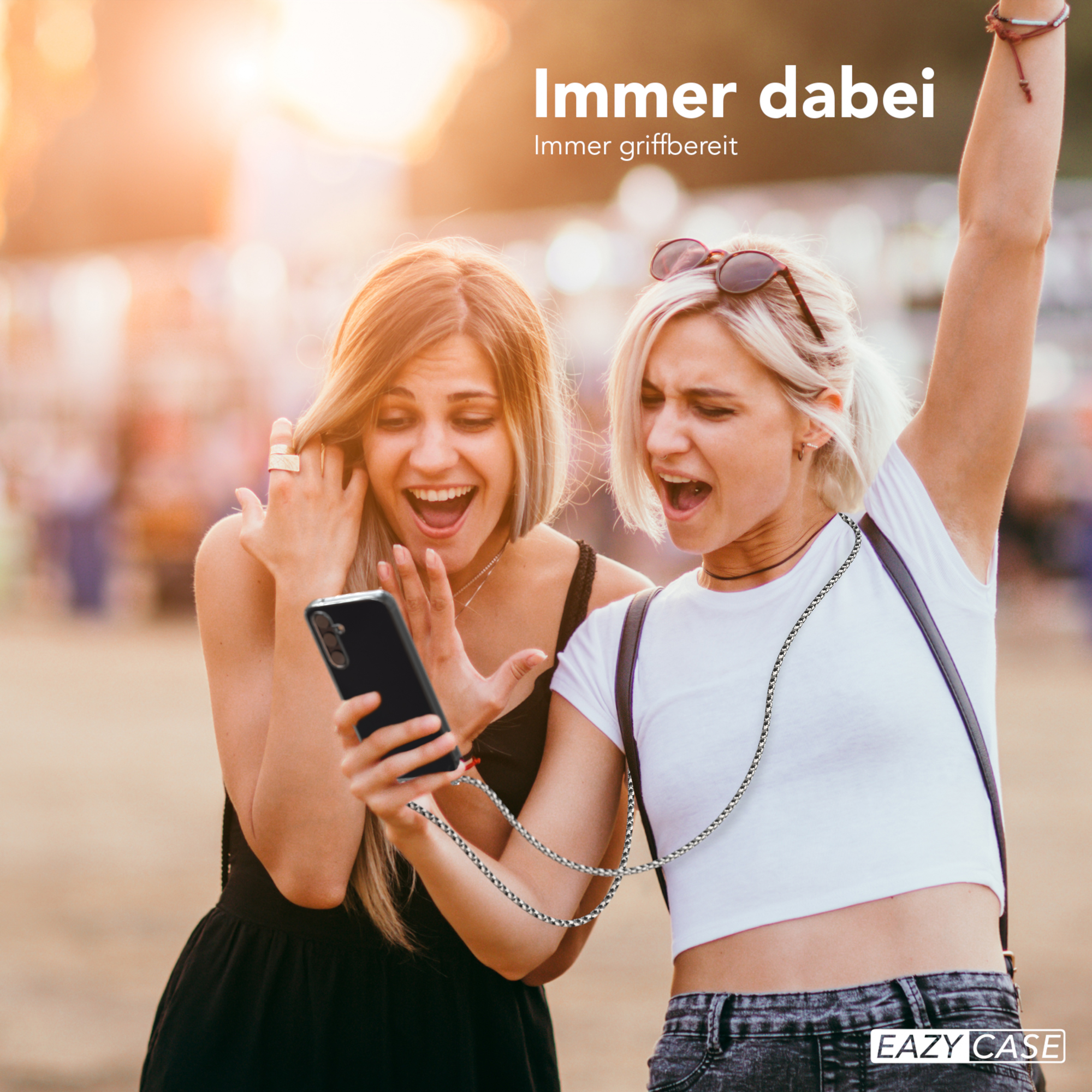 Zwei Frauen schauen auf ein Telefon mit Riemen. Sonnige Szene im Freien.