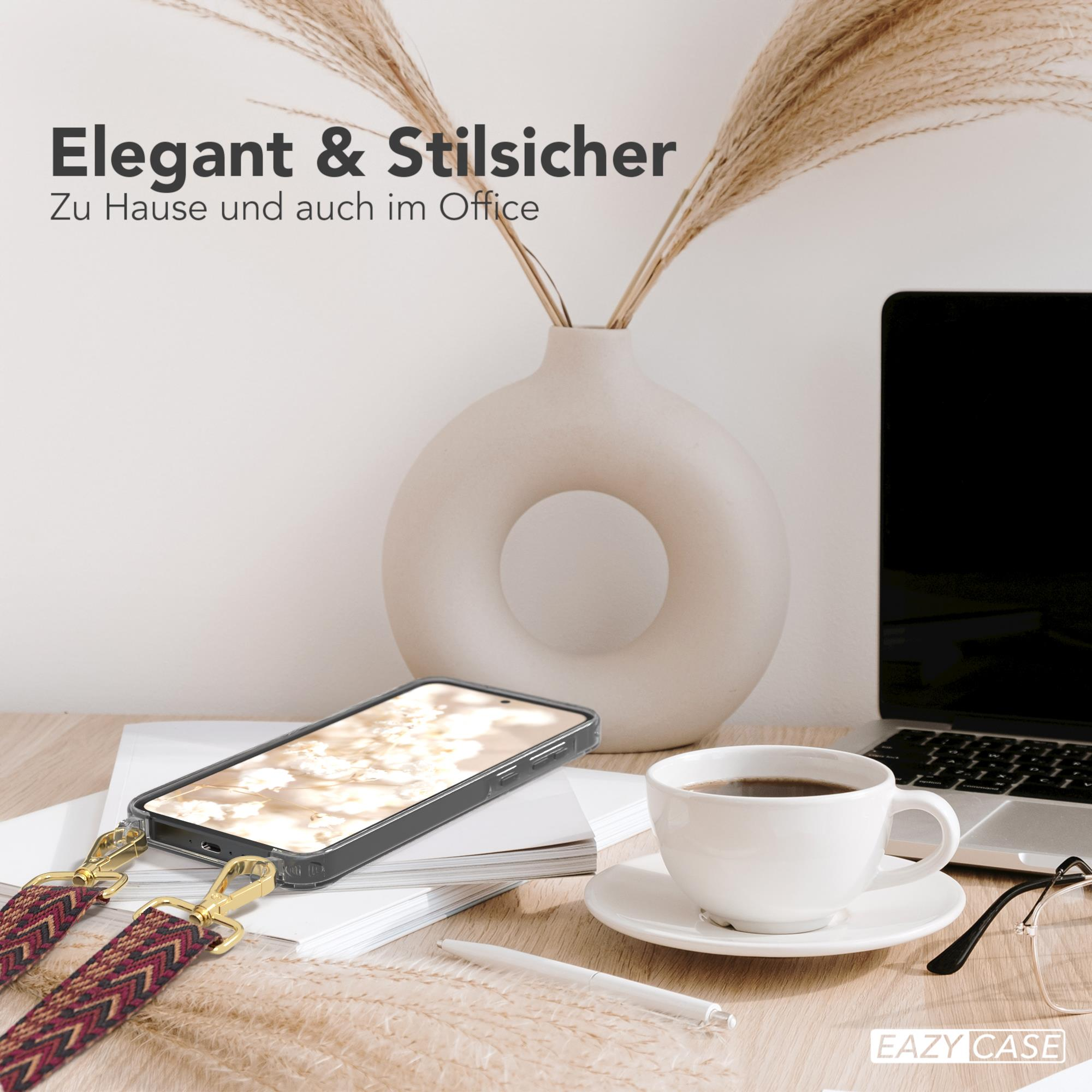 Ein Telefon in einer Hülle mit Trageriemen auf einem Schreibtisch. Kaffee, Laptop, Brille und Vase sind im Bild.