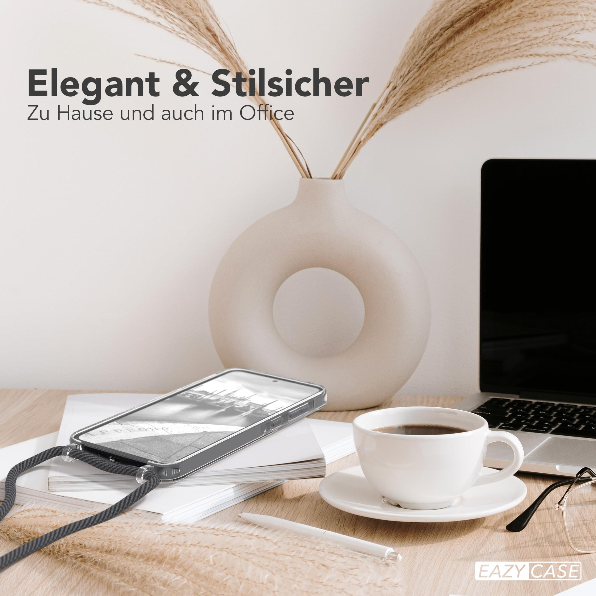 Telefon mit Riemen liegt auf Tisch mit Kaffee, Stift und Laptop. Vase mit Pflanzen im Hintergrund.