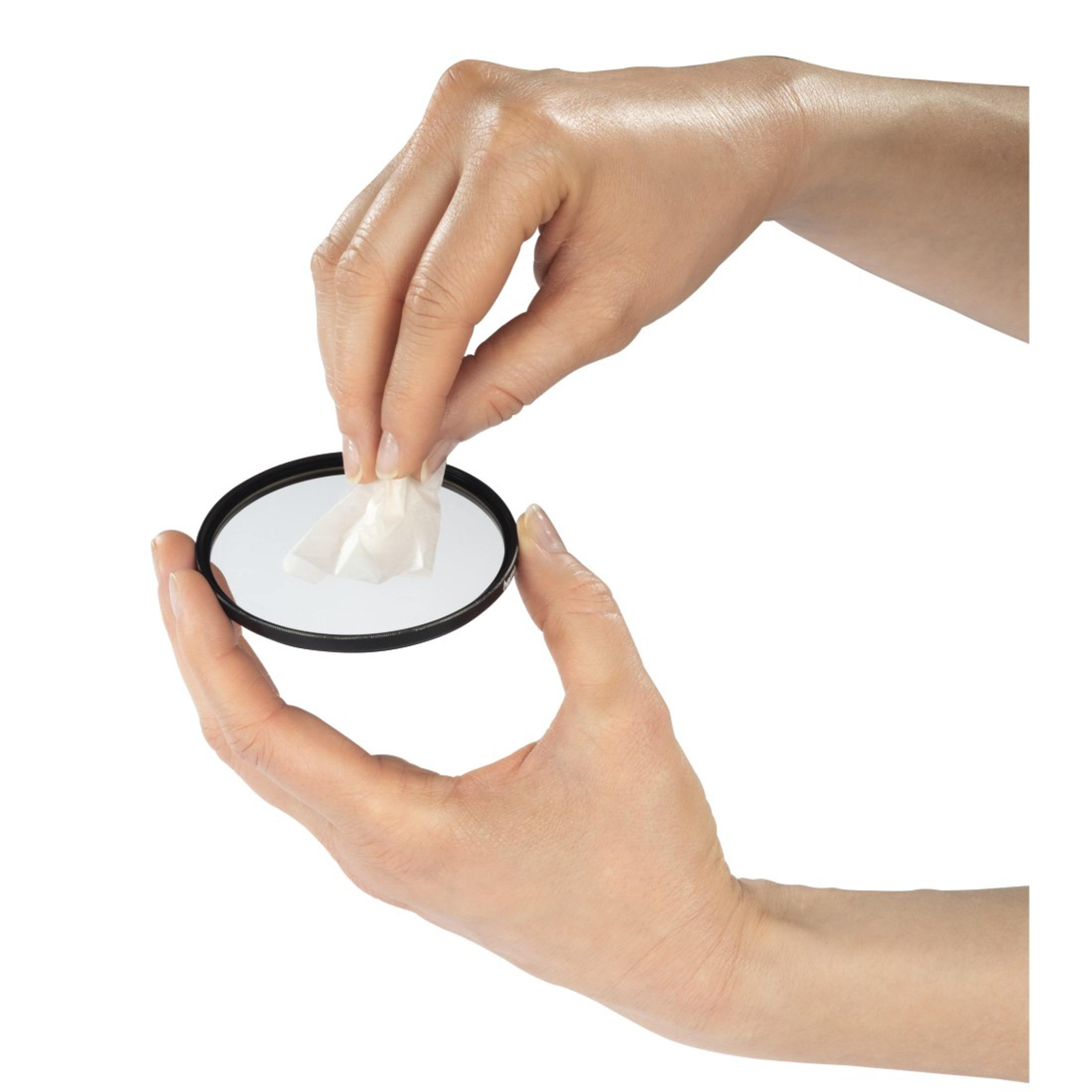 Dłoń trzymająca filtr obiektywu i wycierająca go chusteczką. Skupienie na obiektywie i działaniach dłoni.