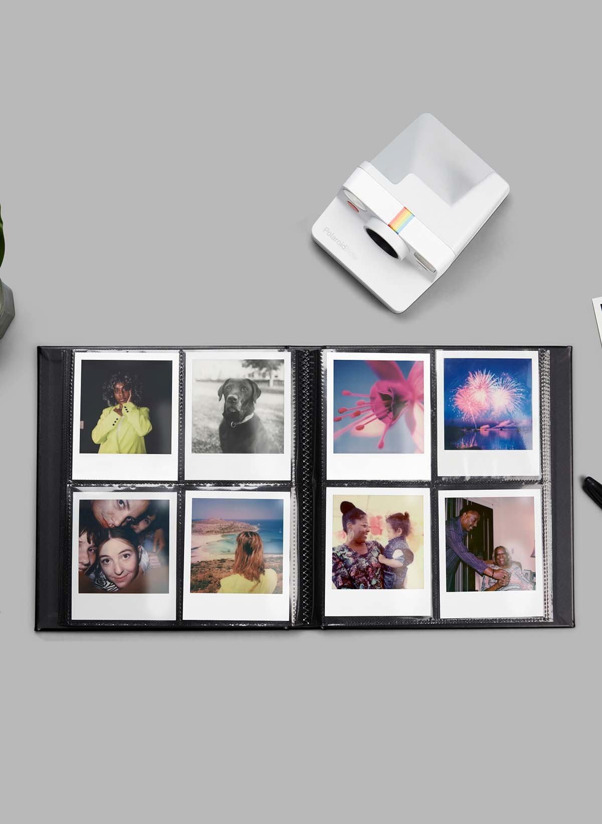 Polaroid-Kamera mit Fotoalbum voller Fotos auf grauer Oberfläche.