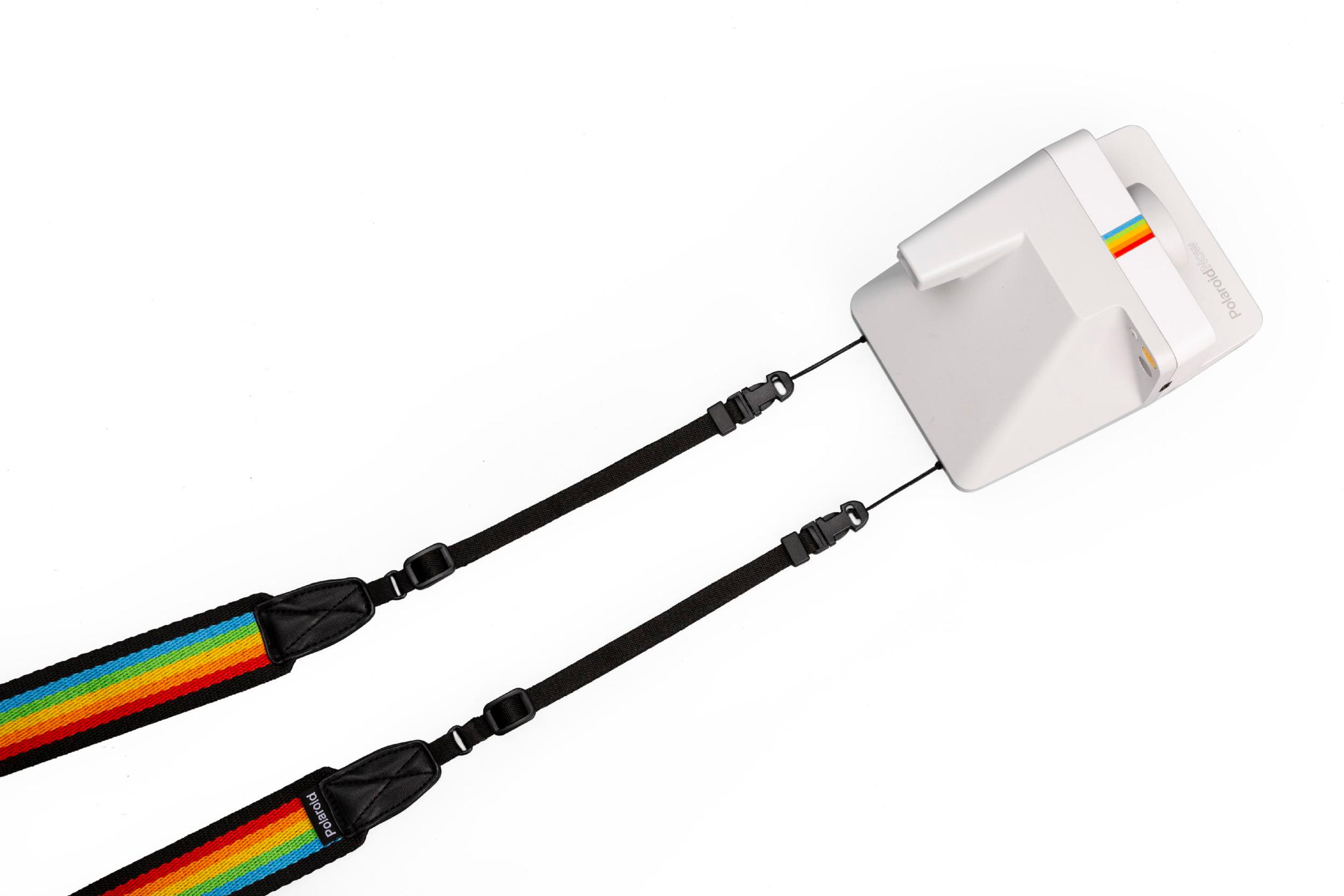 Biały aparat Polaroid z dołączonym paskiem w tęczowych barwach, na białym tle.