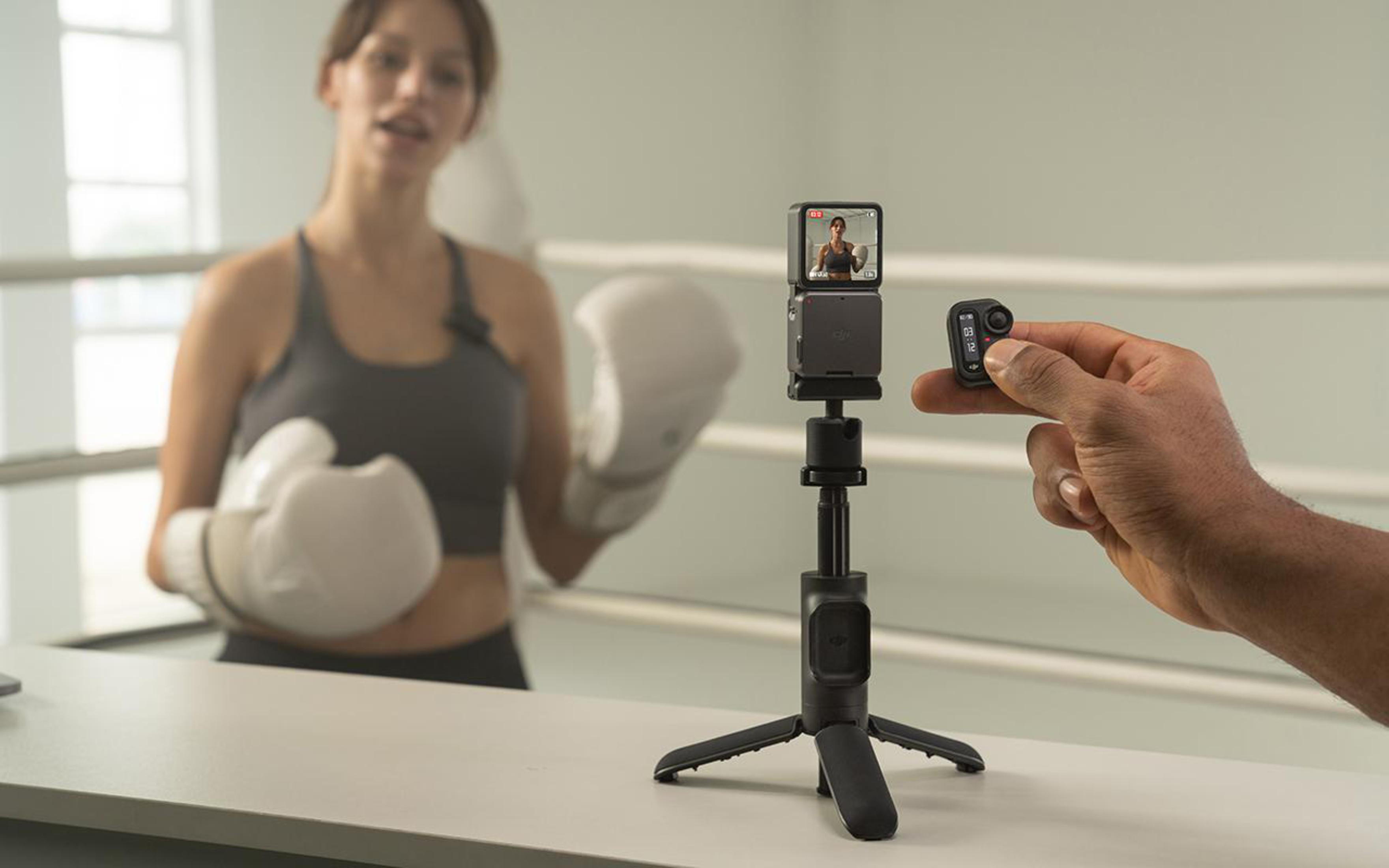 Person filmen mit kleiner Kamera auf Stativ, Boxer im Hintergrund.