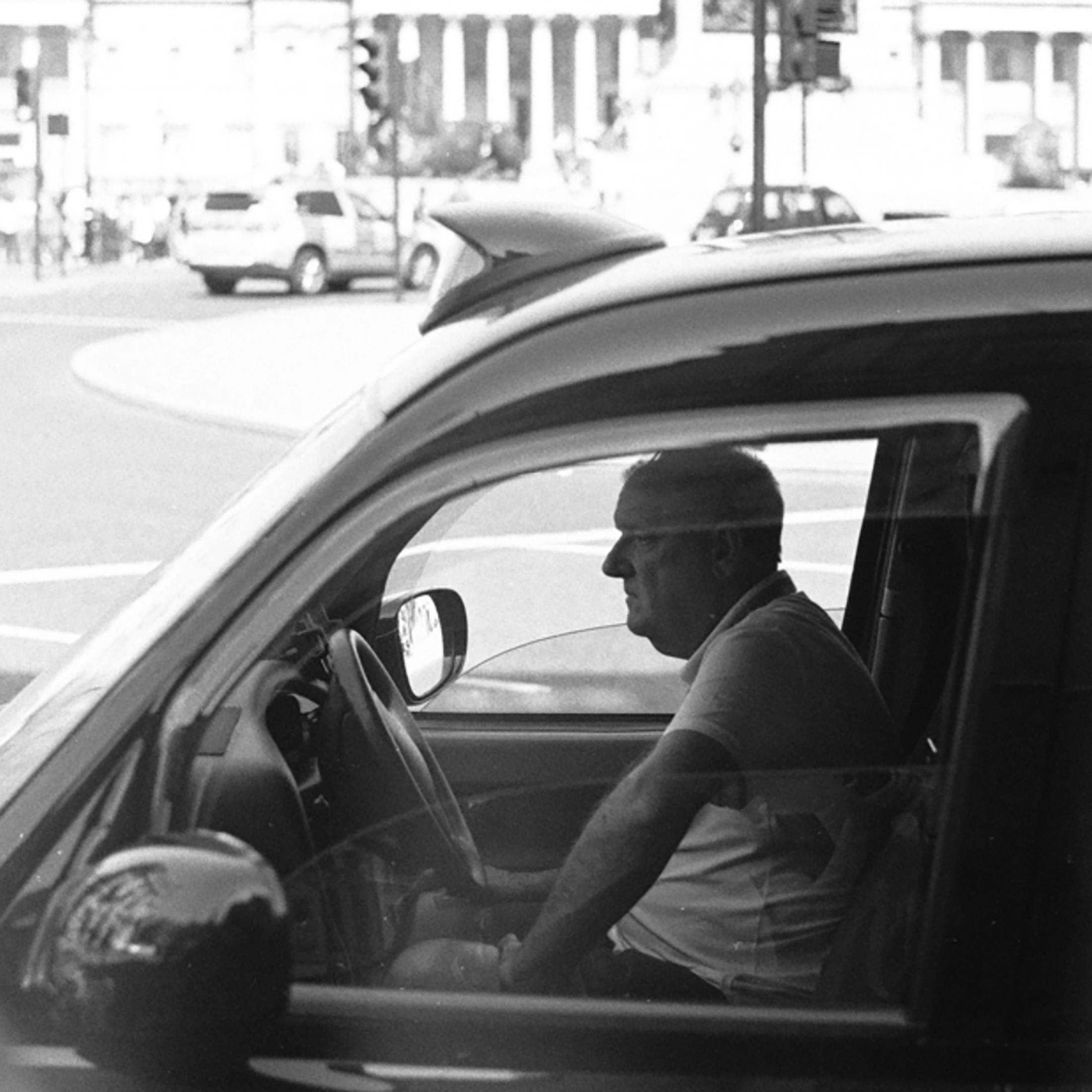 Mann fährt ein schwarzes Taxi. Die Szene ist in Graustufen mit unscharfem Hintergrund.