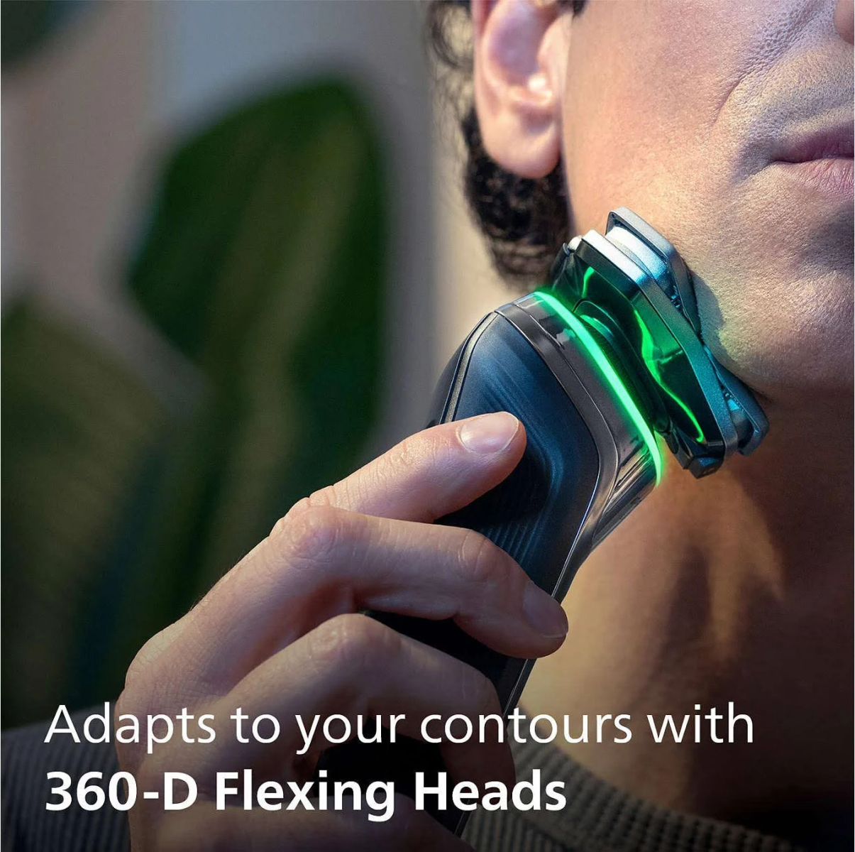 Mężczyzna goli się czarno-srebrną golarką elektryczną. Zielone światło na głowicy.