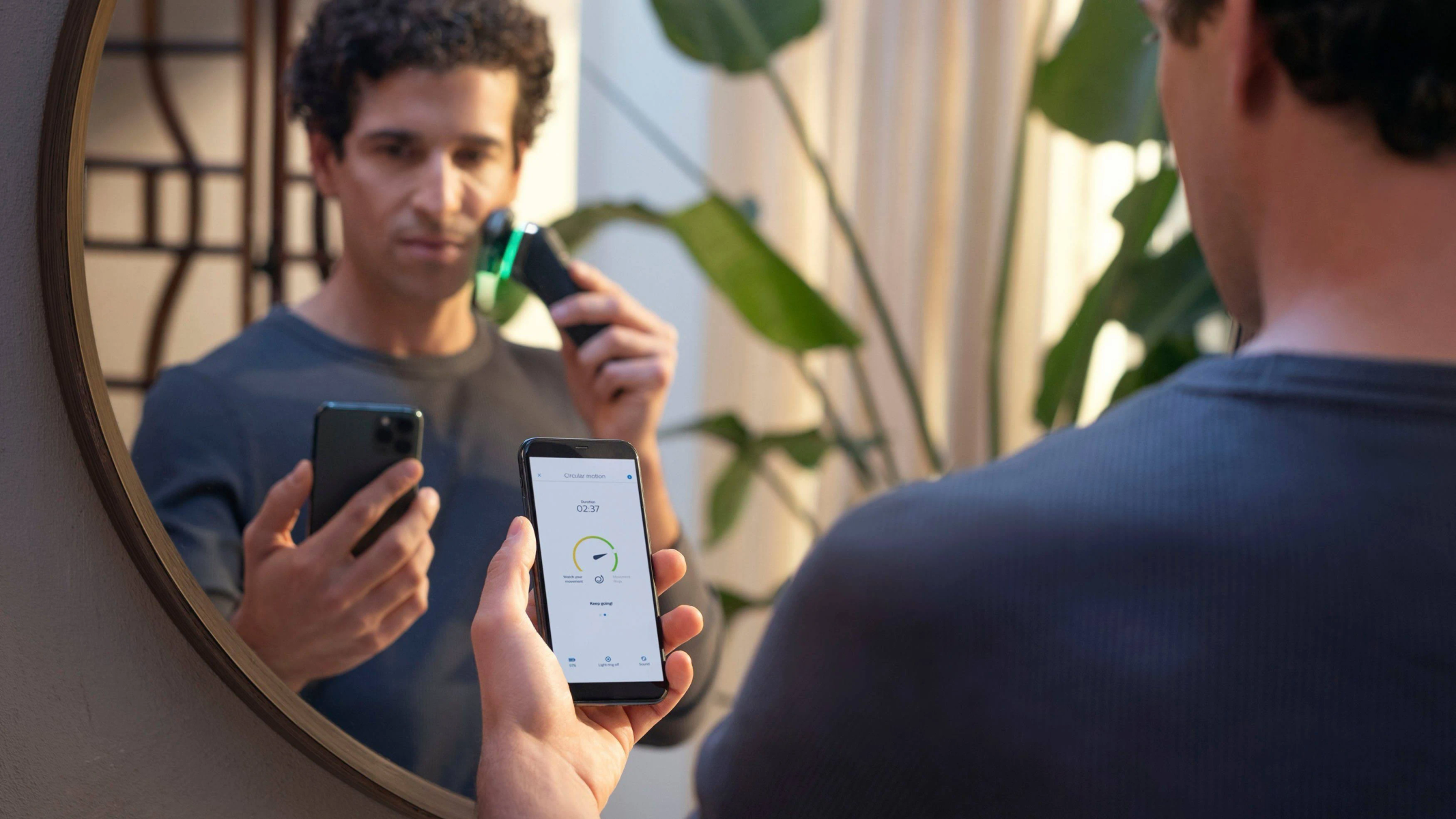 Mężczyzna goli się przed lustrem, patrząc na telefon. Telefon pokazuje postęp golenia.