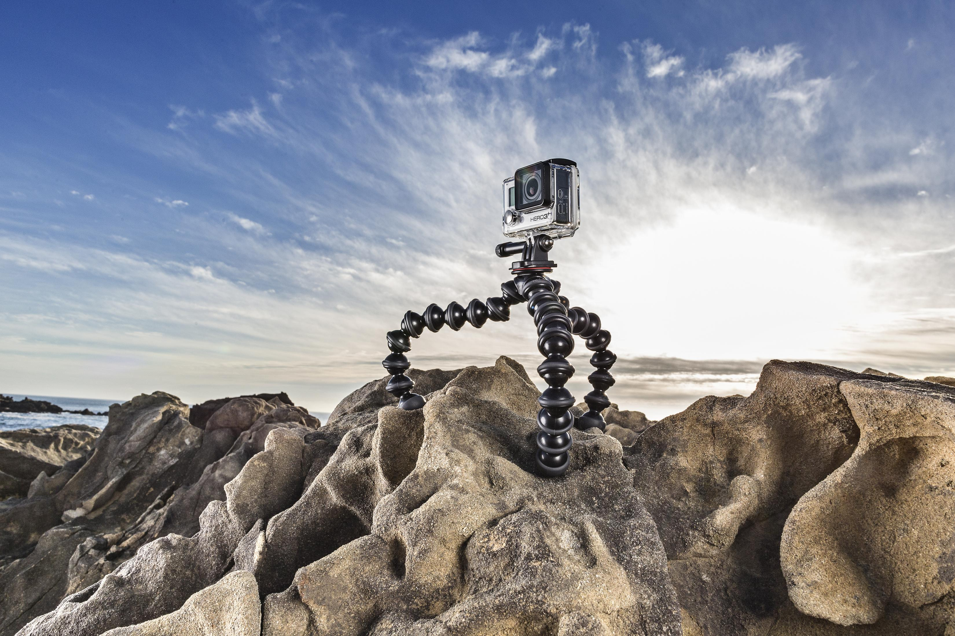 Una fotocamera nera è montata su un treppiede flessibile su una roccia con sfondo di cielo blu.