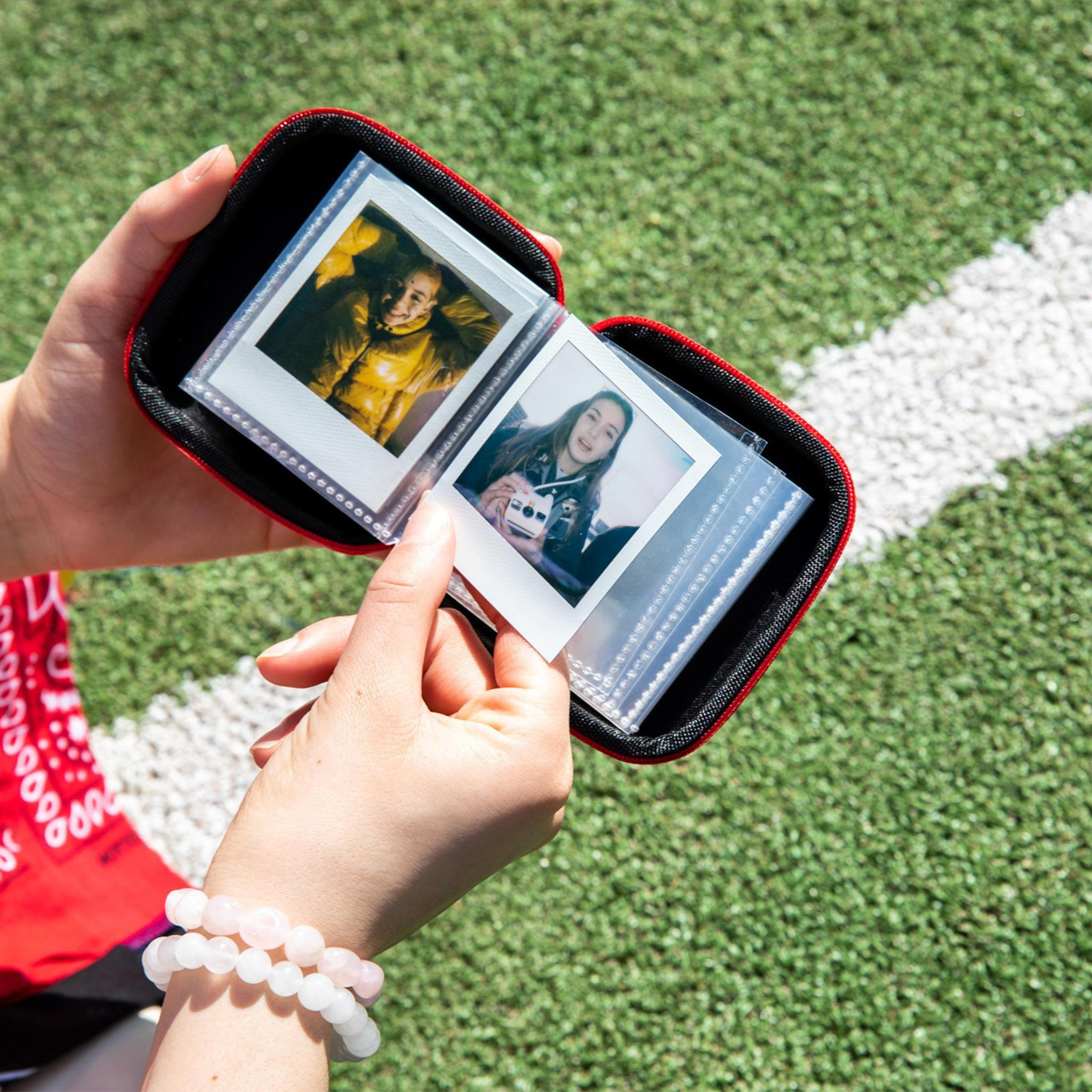 Eine Person hält ein Fotoalbum mit zwei Fotos darin, auf grünem Gras.