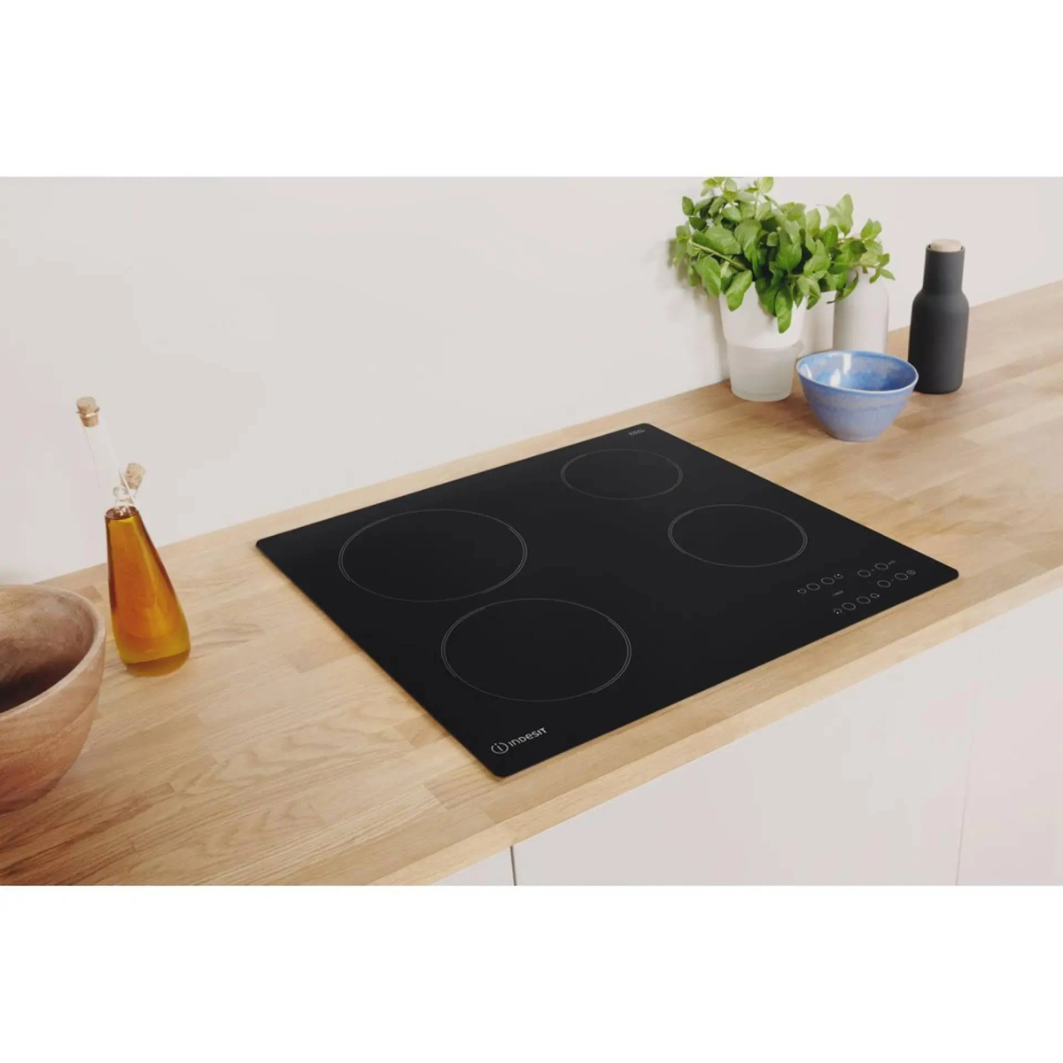 Placa de inducción negra sobre superficie de madera. Cuatro quemadores circulares con controles táctiles.