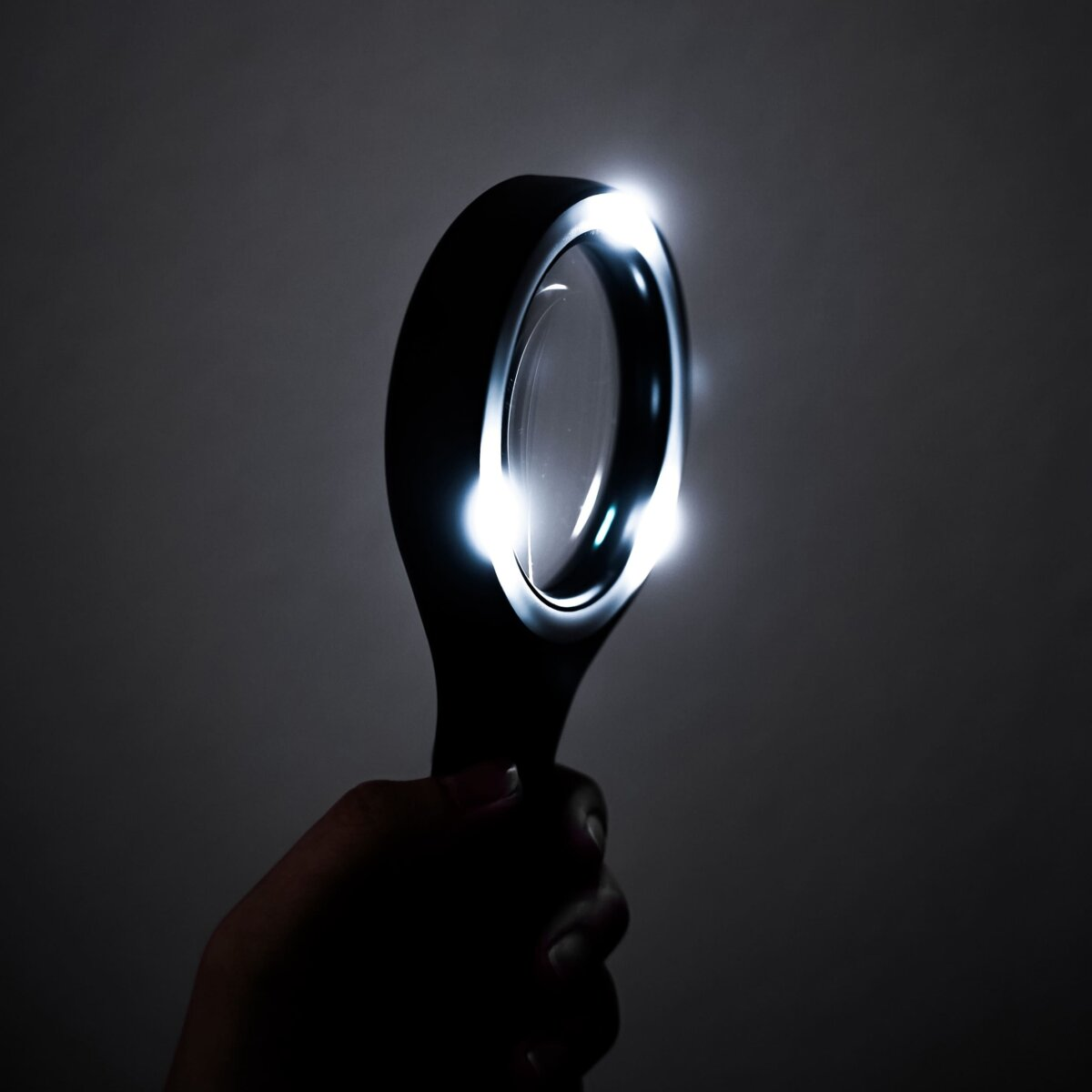 Hand hält eine schwarze Lupe mit hellem LED-Licht, das die Linse beleuchtet.