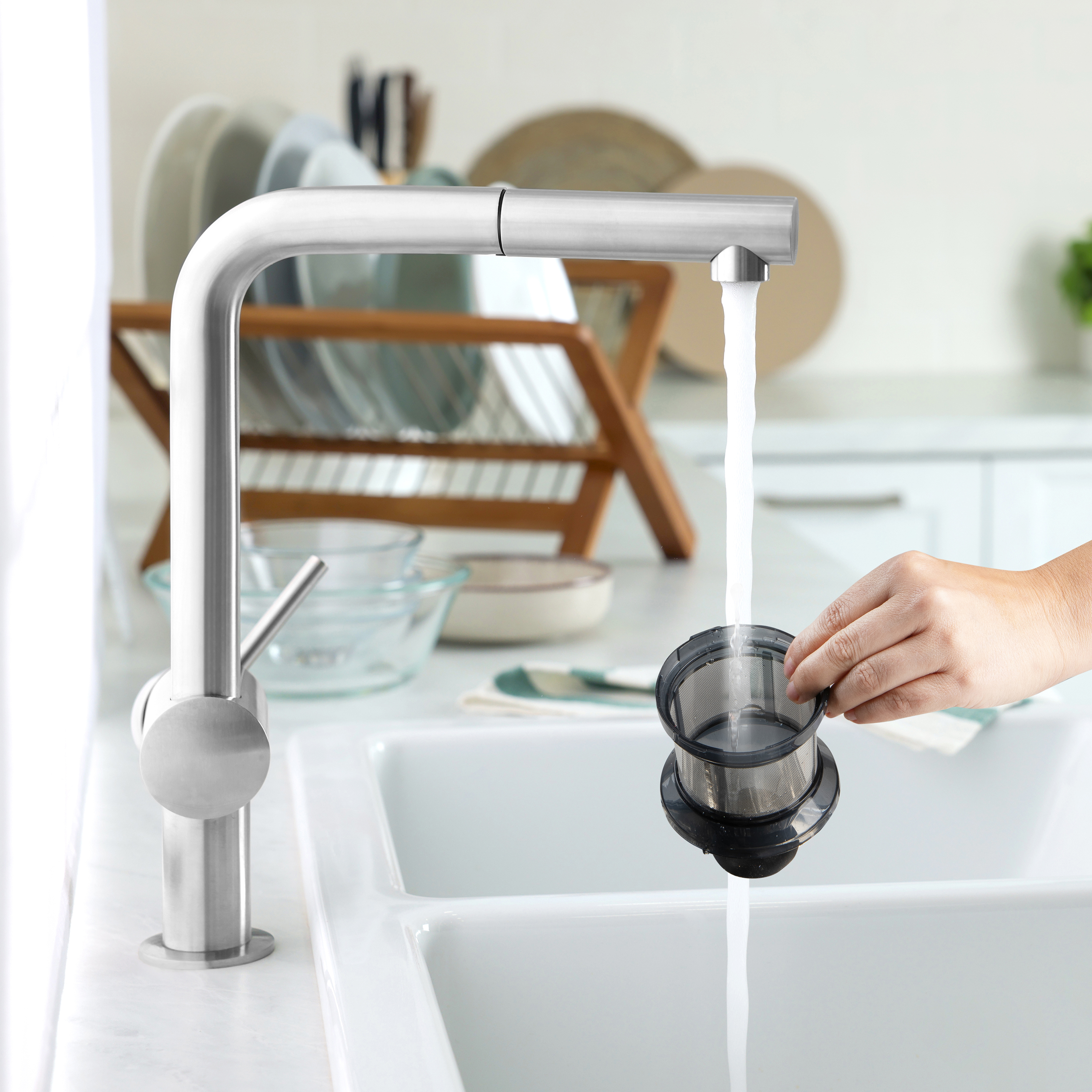 Hand hält schwarzen Filter unter silberner Armatur. Weißes Waschbecken und Hintergrund.