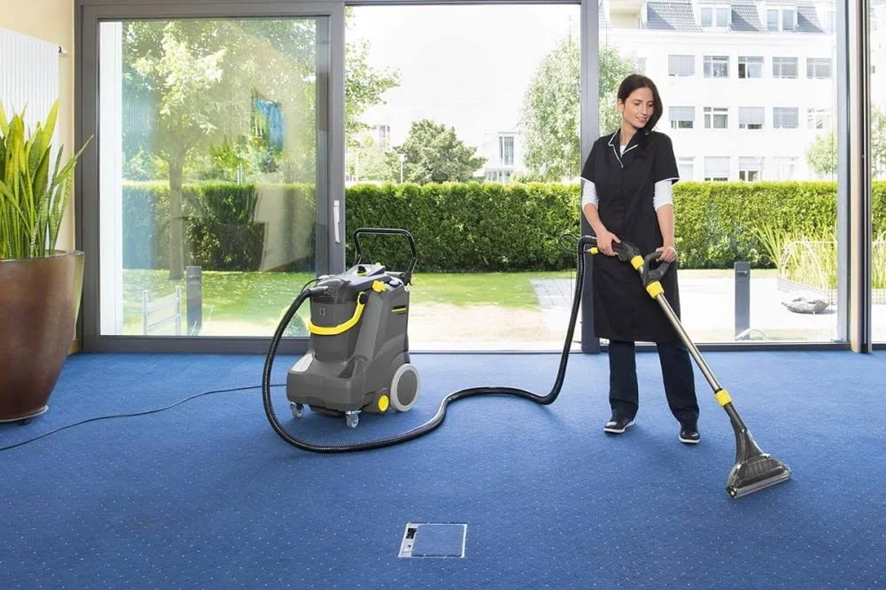 Donna che pulisce un tappeto blu con un aspirapolvere in un ambiente ufficio.
