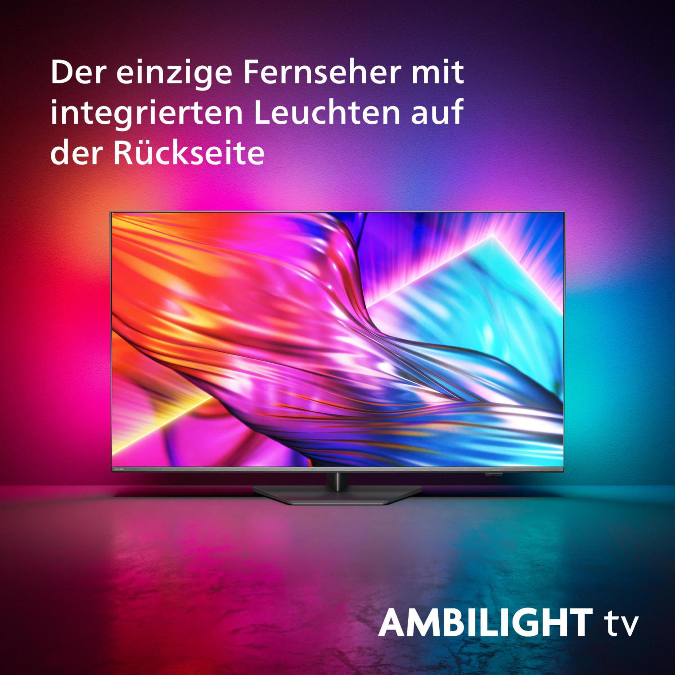 Moderner Fernseher mit farbenfroher Hintergrundbeleuchtung. Der Bildschirm zeigt helle Farben. Er steht auf dunkler Oberfläche.