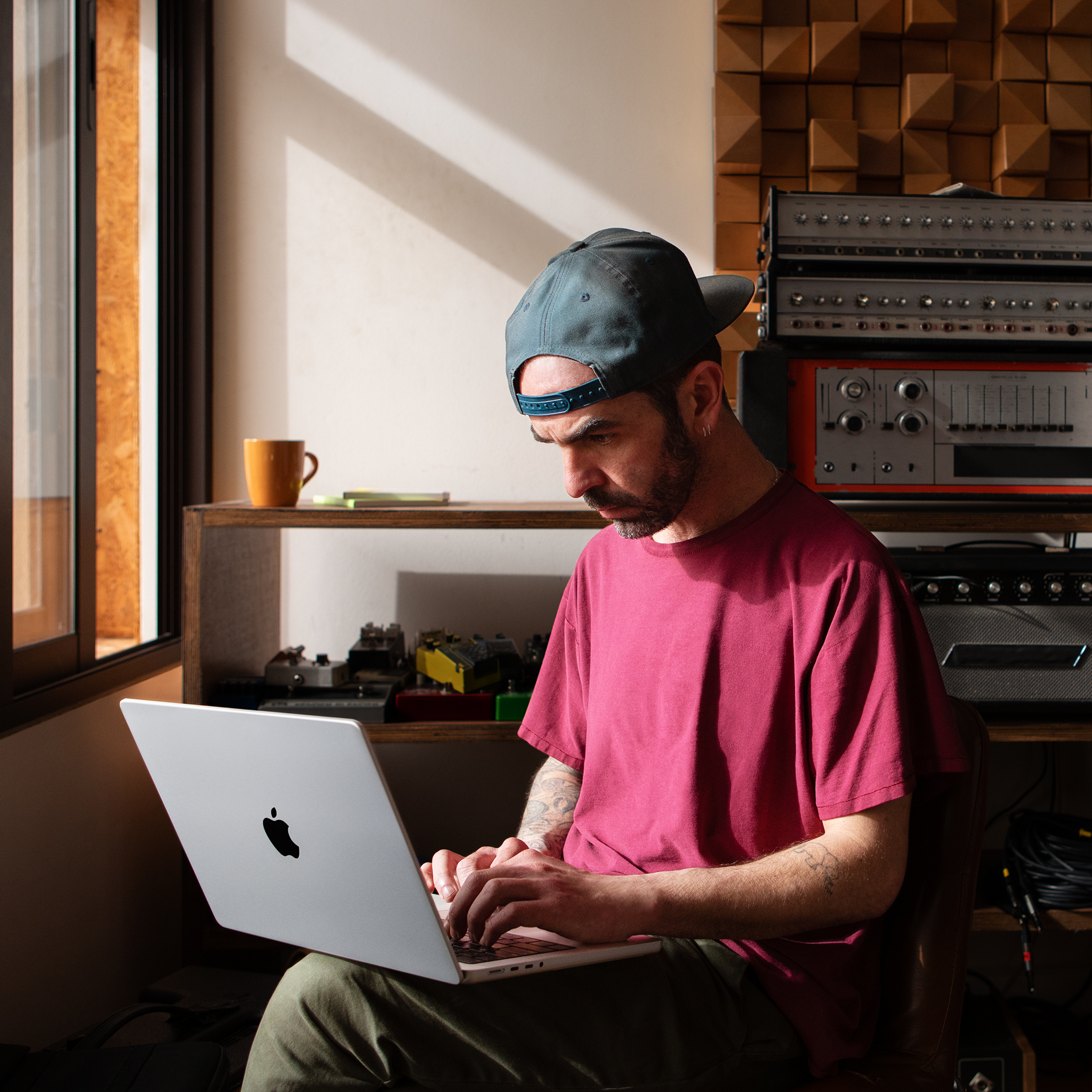 Ein Mann mit Mütze arbeitet an einem Laptop. Er ist in einem Raum mit Holzverkleidung und Tontechnik.