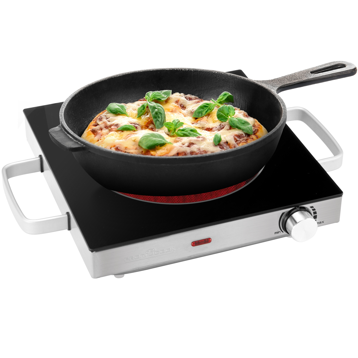 Pizza w czarnej żeliwnej patelni na czarno-srebrnej kuchence elektrycznej. Liście bazylii na wierzchu.