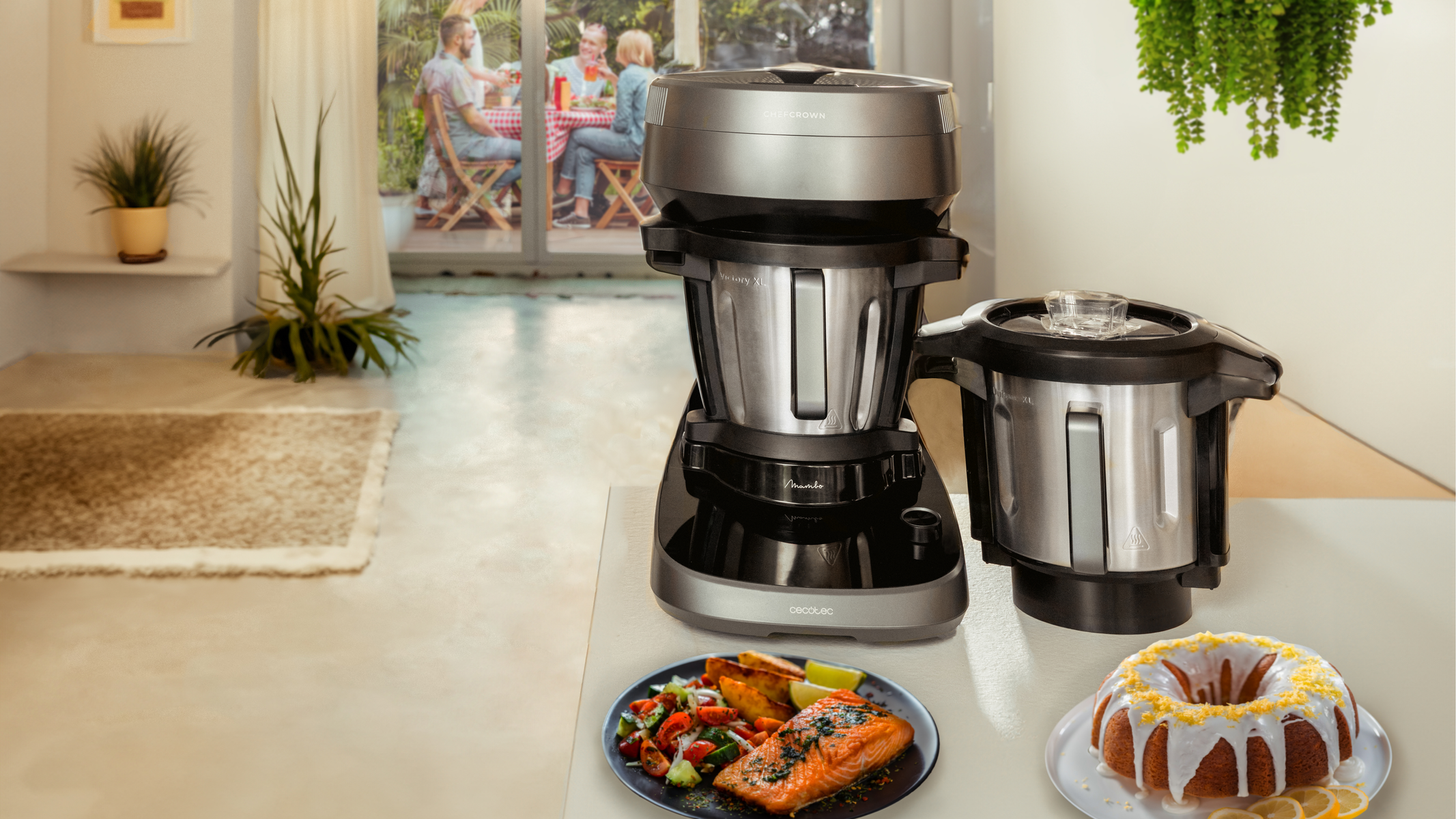 Scena della cucina. Un robot da cucina e una torta sono sul bancone. Ci sono persone sullo sfondo.