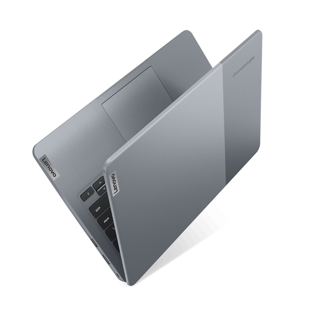 Una laptop Lenovo Chromebook Plus gris está abierta sobre un fondo negro. Se ven el teclado, el panel táctil y la pantalla.
