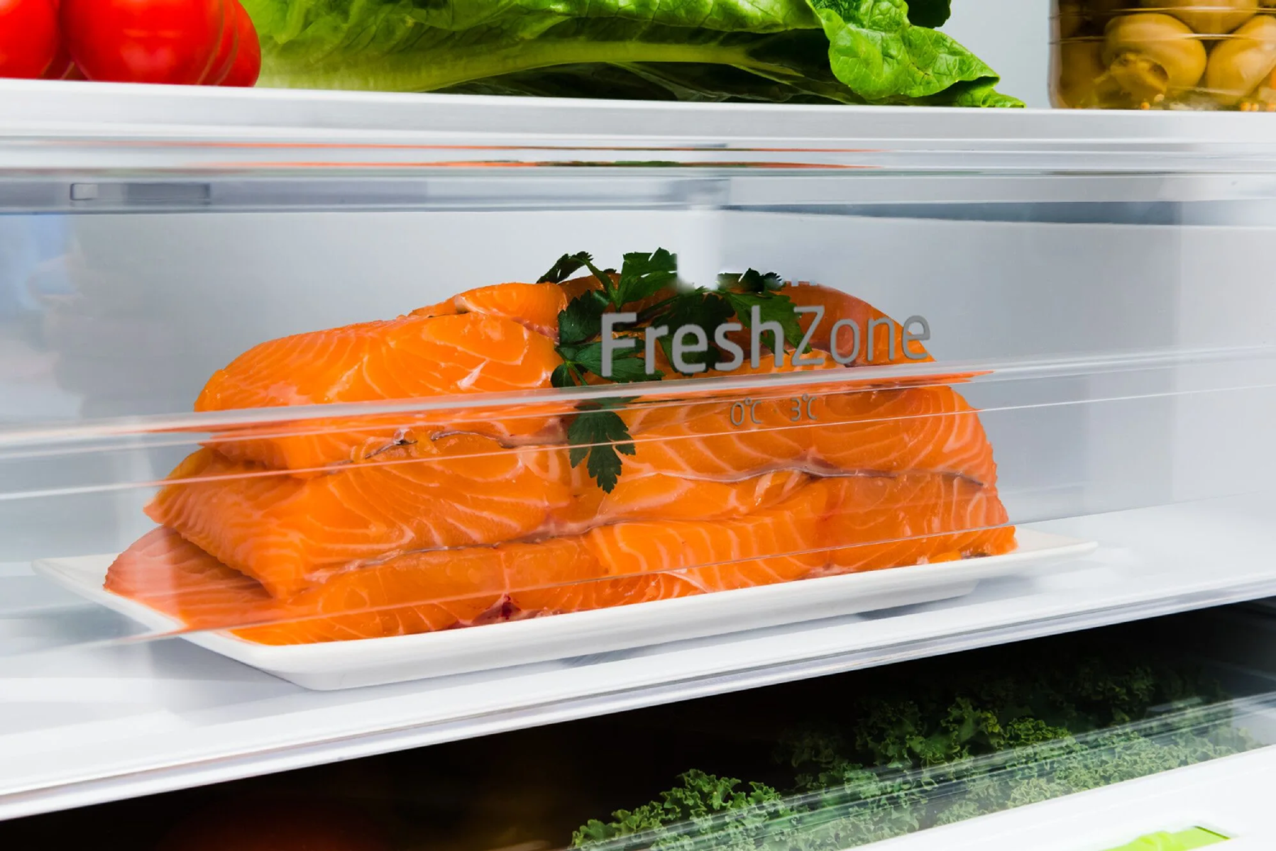 Wnętrze lodówki z filetami z łososia na białym talerzu, z napisem 'FreshZone'.