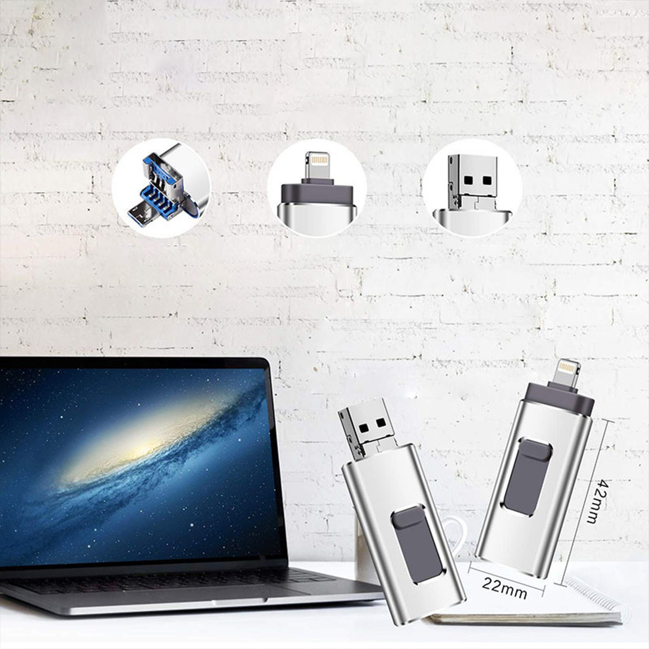 Zwei silberne USB-Laufwerke auf einem Tisch, mit einem Laptop im Hintergrund. Weiße Wand.