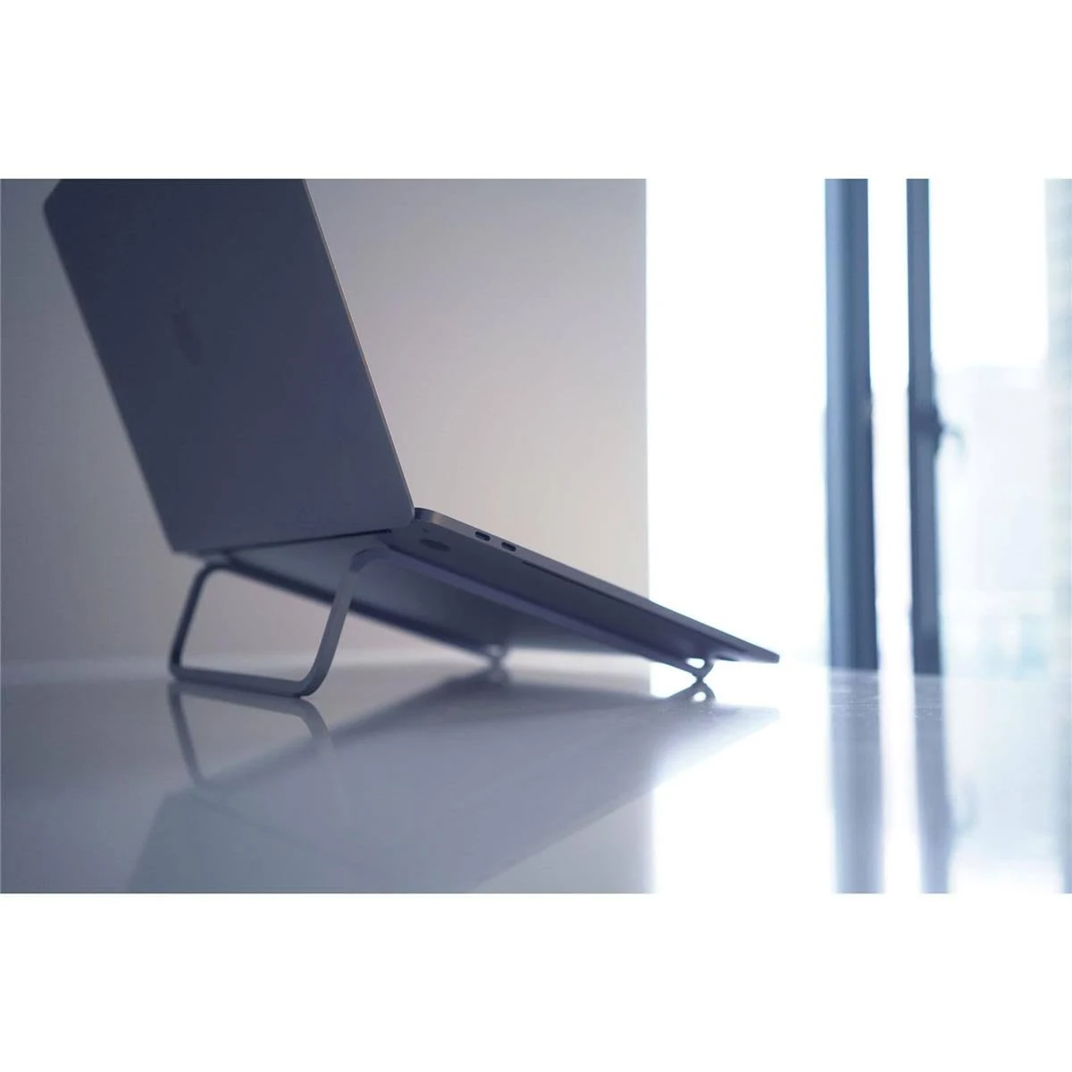 Laptop auf einem grauen Ständer auf weißer Oberfläche, in der Nähe eines Fensters. Heller Hintergrund.