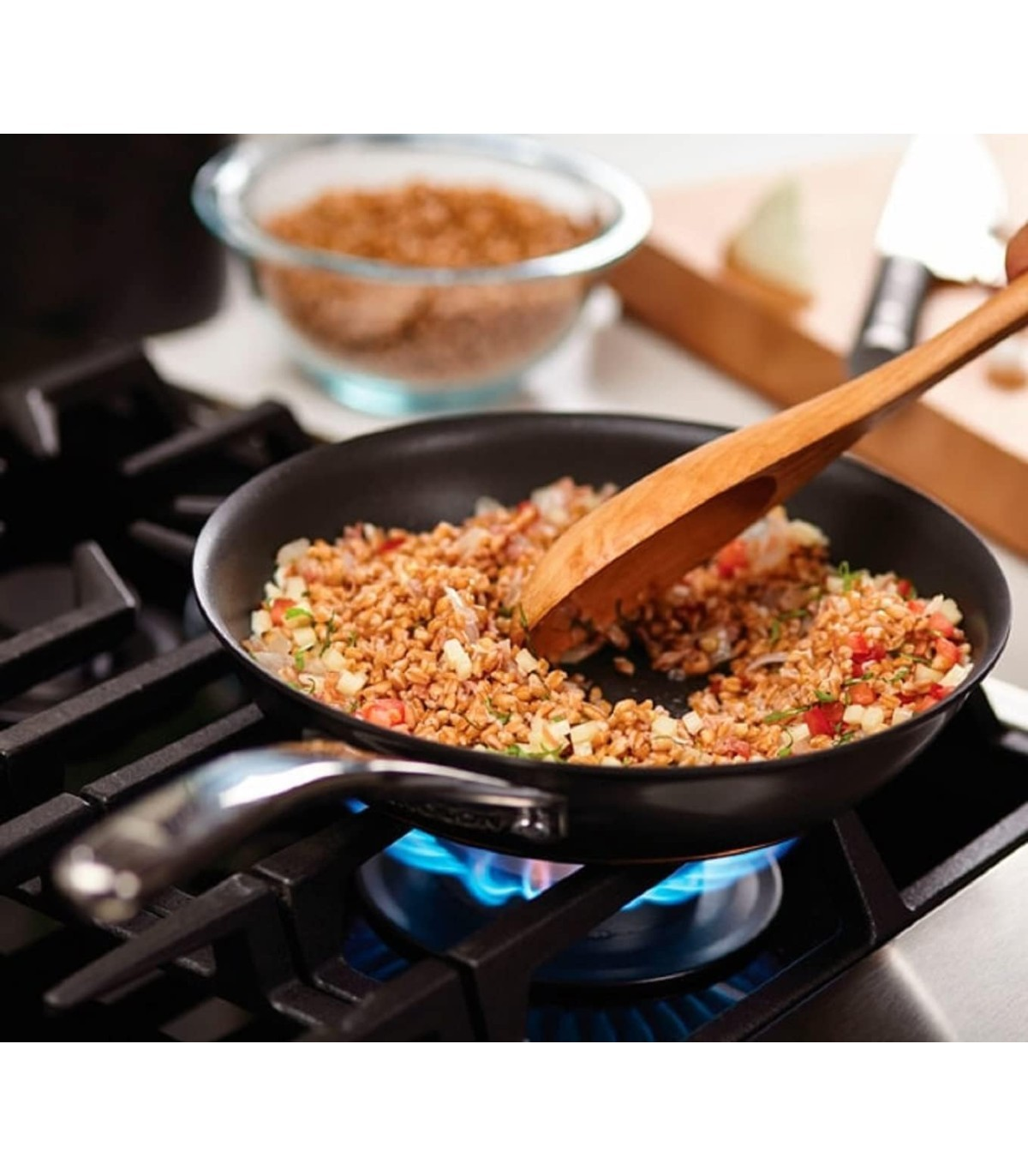 Se muestra una sartén con comida cocinándose en una estufa de gas, junto con una cuchara de madera.