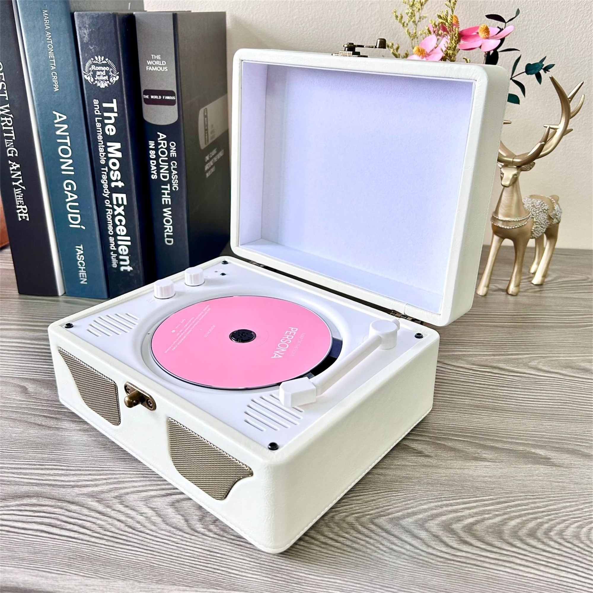 Weißer Plattenspieler mit rosa Schallplatte, neben Büchern und goldener Hirschstatue.