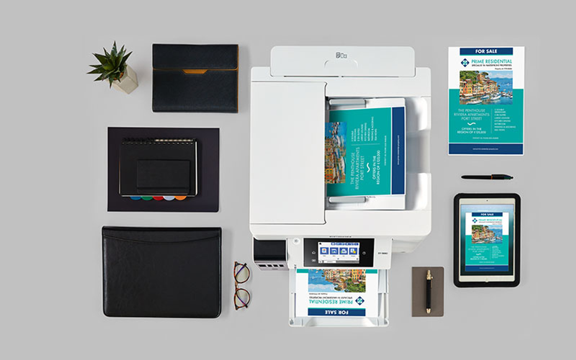 Drukarka z papierami, tabletem, okularami i innymi materiałami biurowymi.