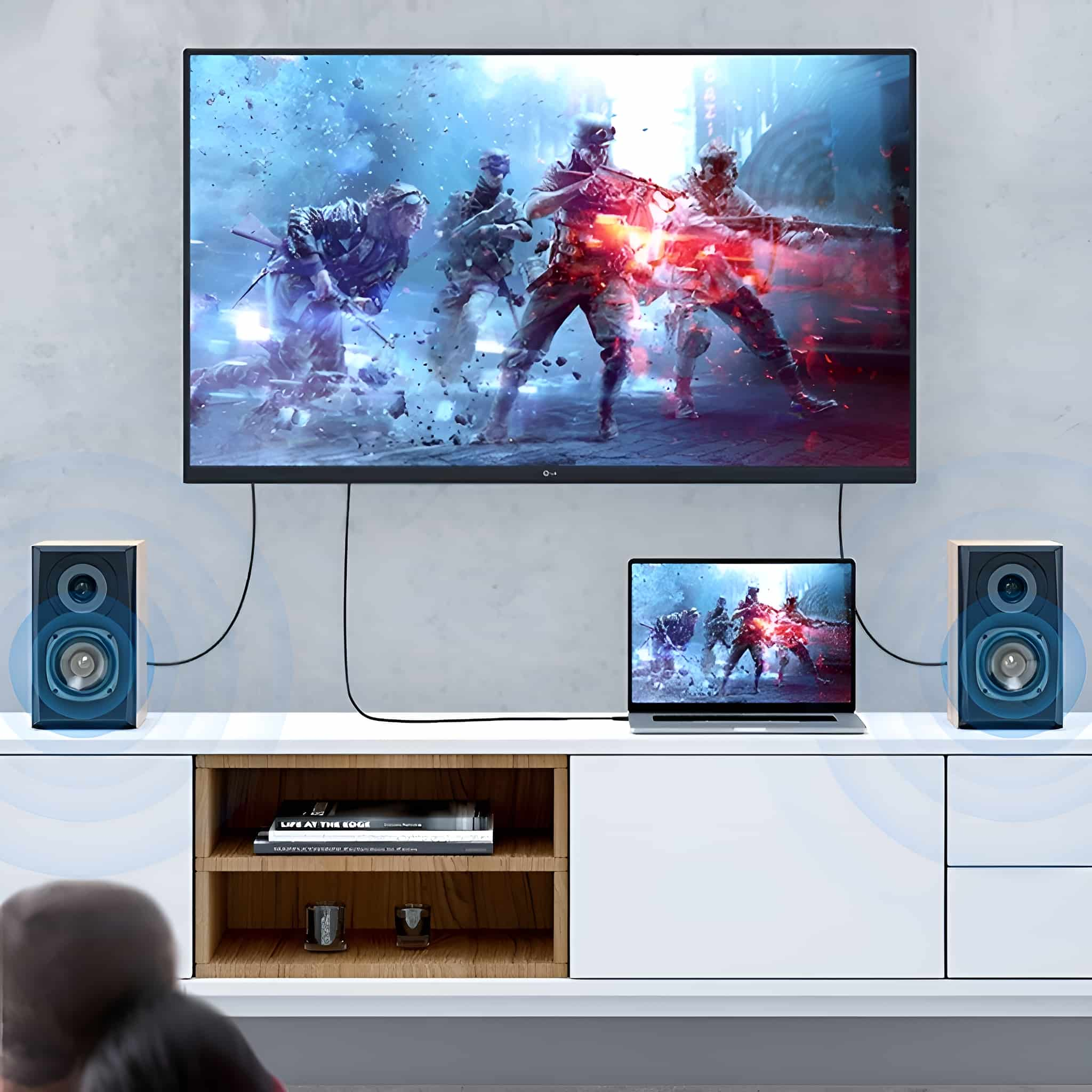 Fernseher mit Videospiel, flankiert von Lautsprechern. Laptop und weißer Schrank sichtbar.