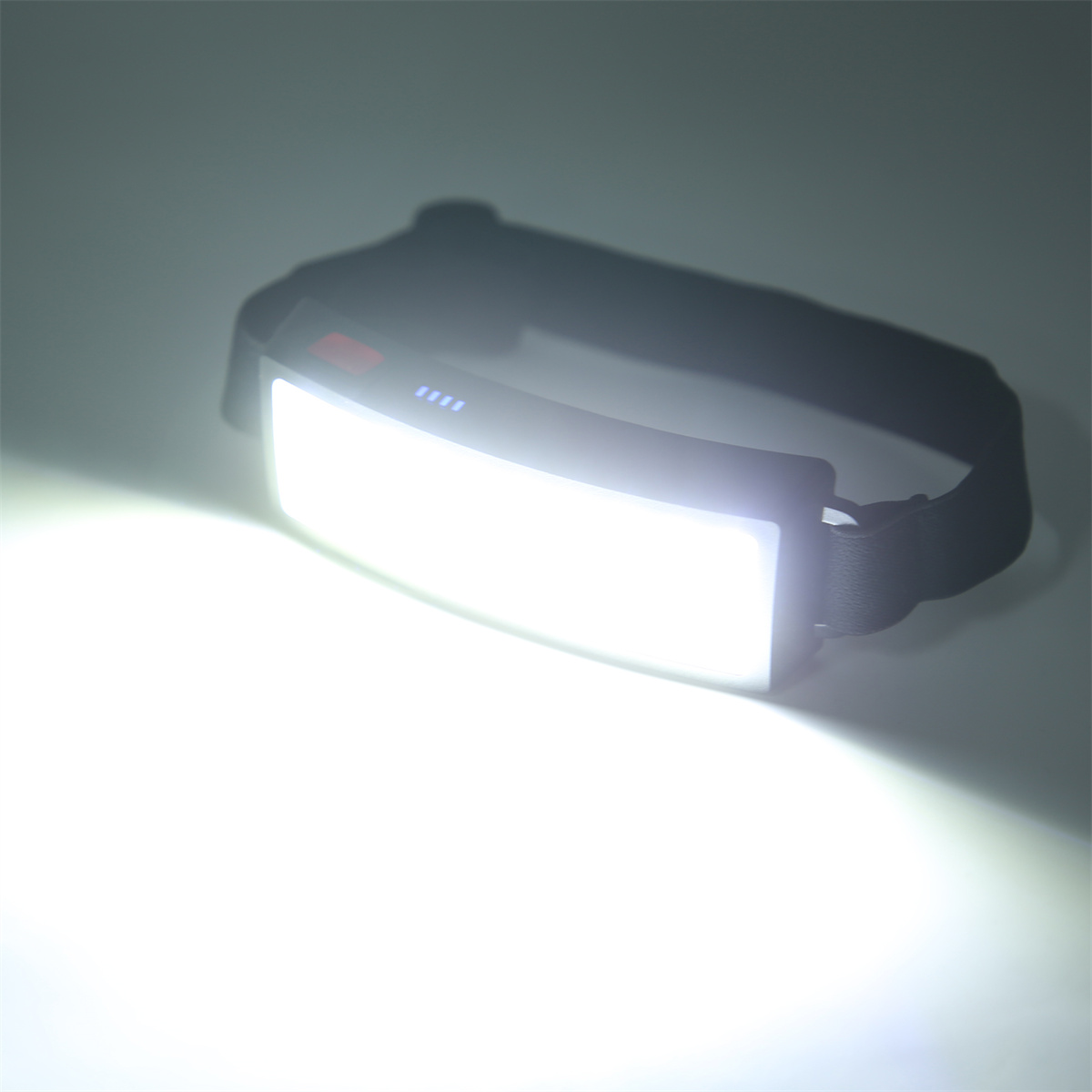 Eingeschaltete Stirnlampe, die ein helles weißes Licht aussendet, auf einer weißen Oberfläche.