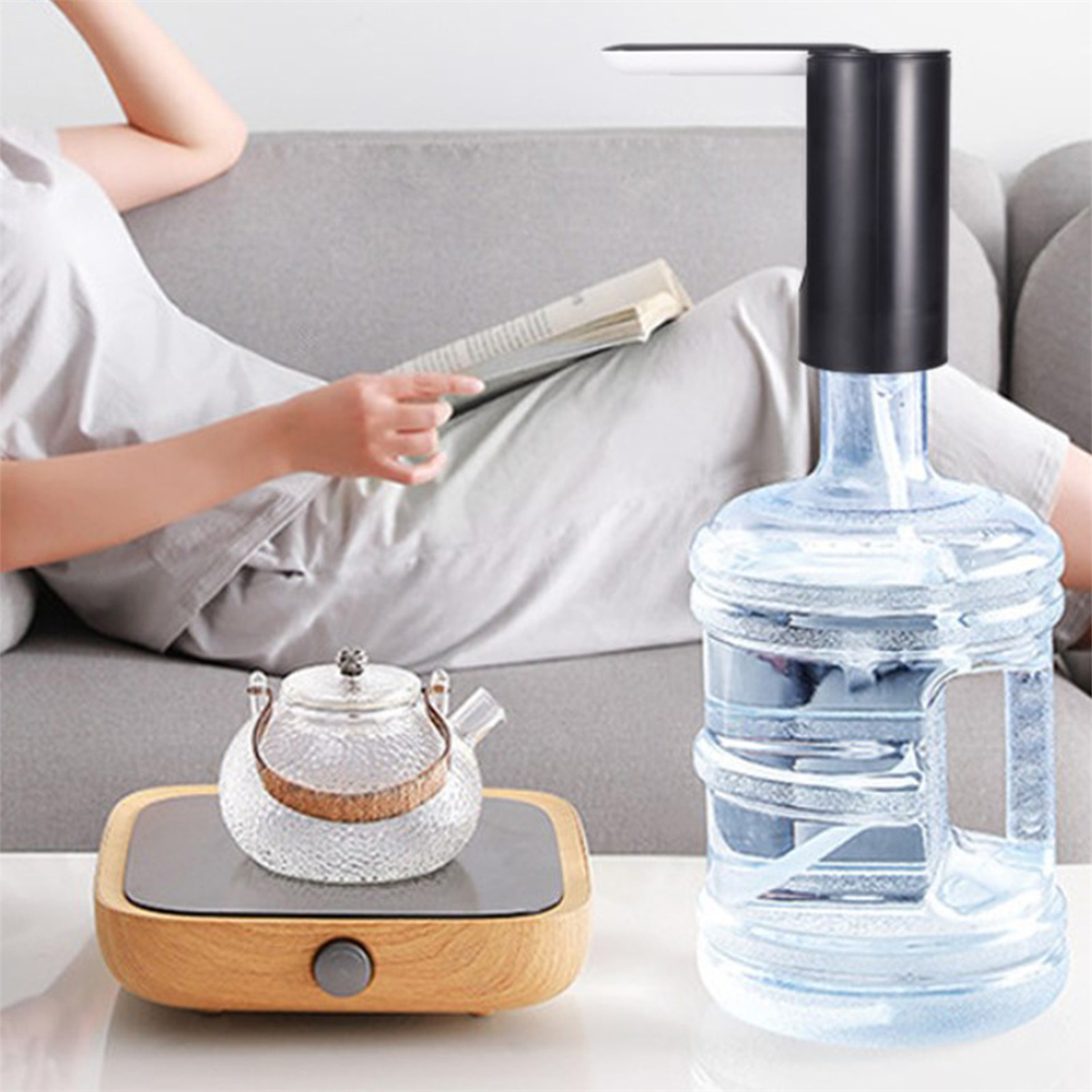 Eine lesende Person, ein Wasserspender auf einer Flasche und eine gläserne Teekanne auf einem Holzkocher.