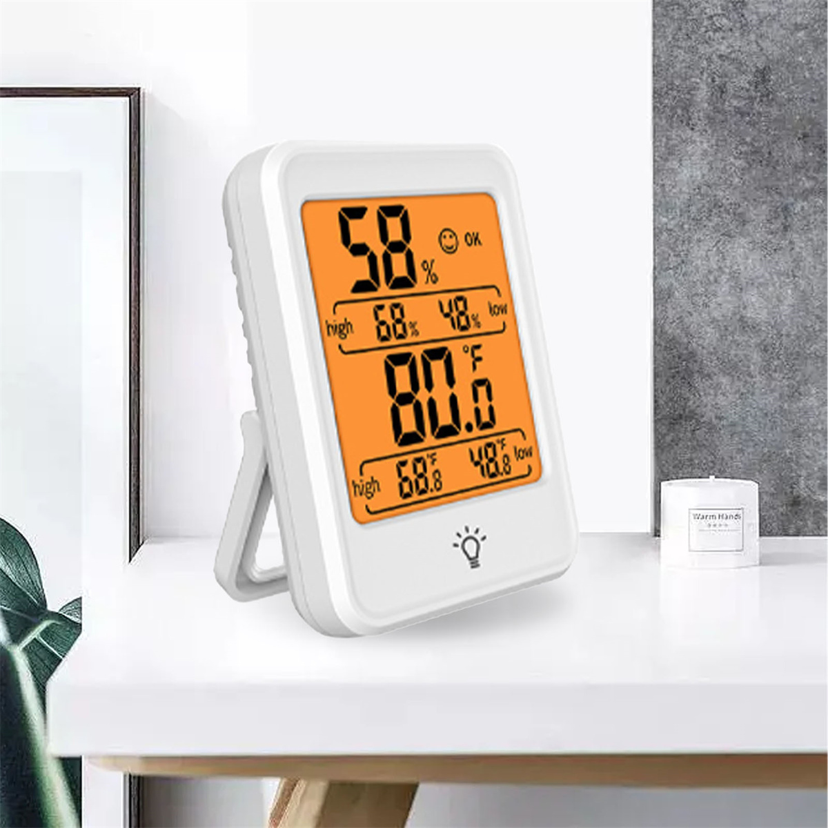 Digitales Thermometer zeigt Temperatur und Luftfeuchtigkeit auf weißem Tisch.