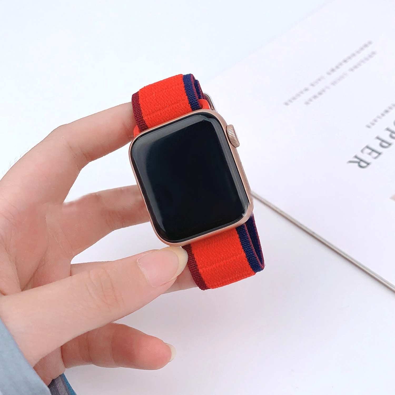 Eine Hand hält eine goldene Apple Watch mit einem rot-blauen Armband.