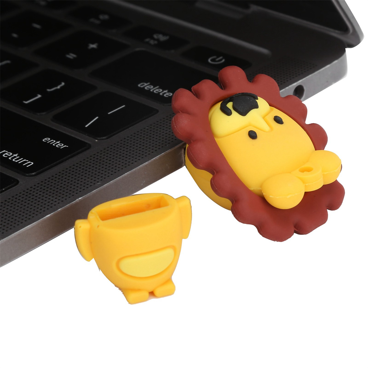 Ein gelber Löwen-USB-Stick mit abgenommener Kappe neben einer Laptop-Tastatur.