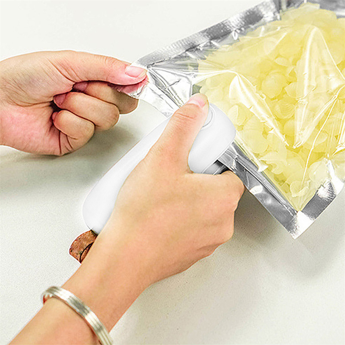 Hände, die einen Plastikbeutel mit einem weißen Handversiegler verschließen. Beutel enthält gelbe Lebensmittel.