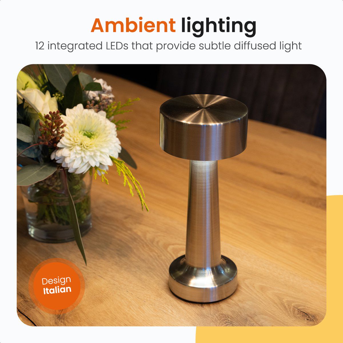 A stainless steel table lamp with ambient lighting and a vase with flowers on a wooden table.