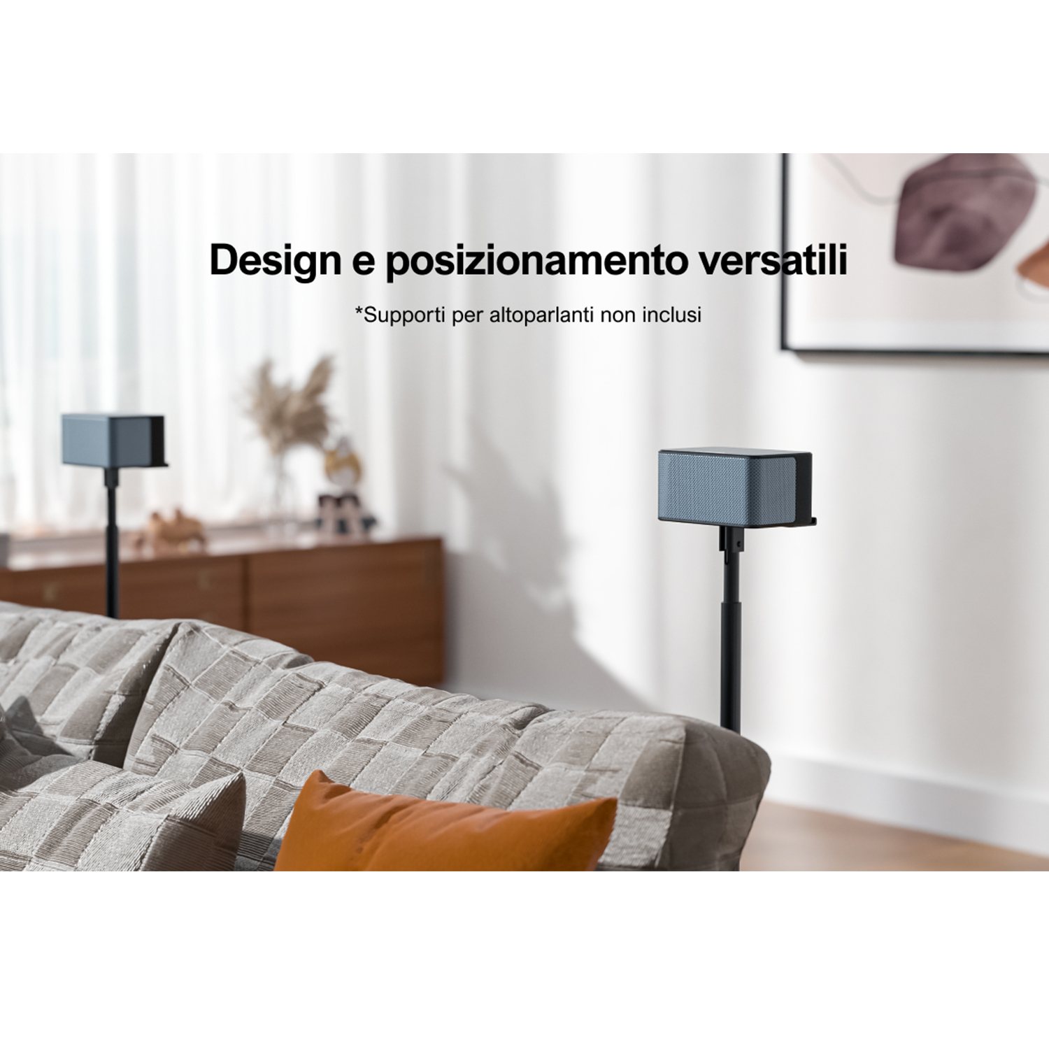 Due altoparlanti neri su supporti in un soggiorno. Un divano grigio e un cuscino arancione in primo piano.