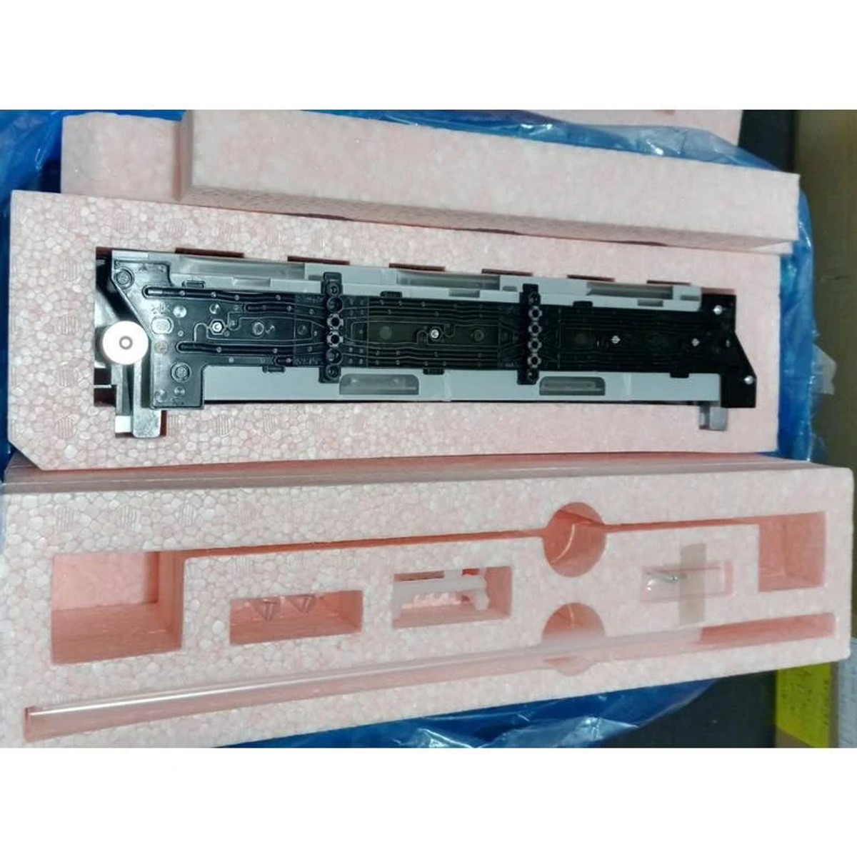 Piezas electrónicas en una caja. Protegidas por espuma rosa. Hay una envoltura de plástico azul.
