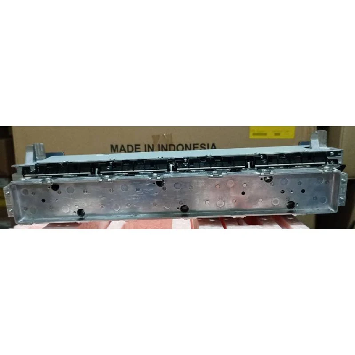 Componente plateado con 'MADE IN INDONESIA' en un fondo de caja de cartón beige.