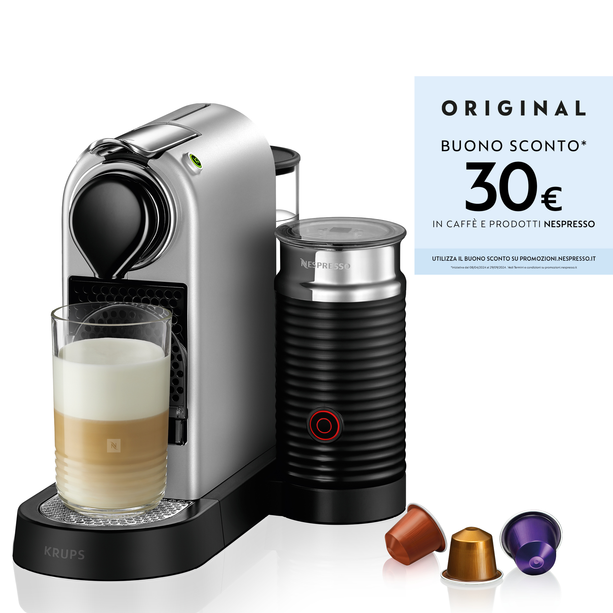 Una macchina Nespresso argentata con montalatte, un bicchiere di latte macchiato e capsule.