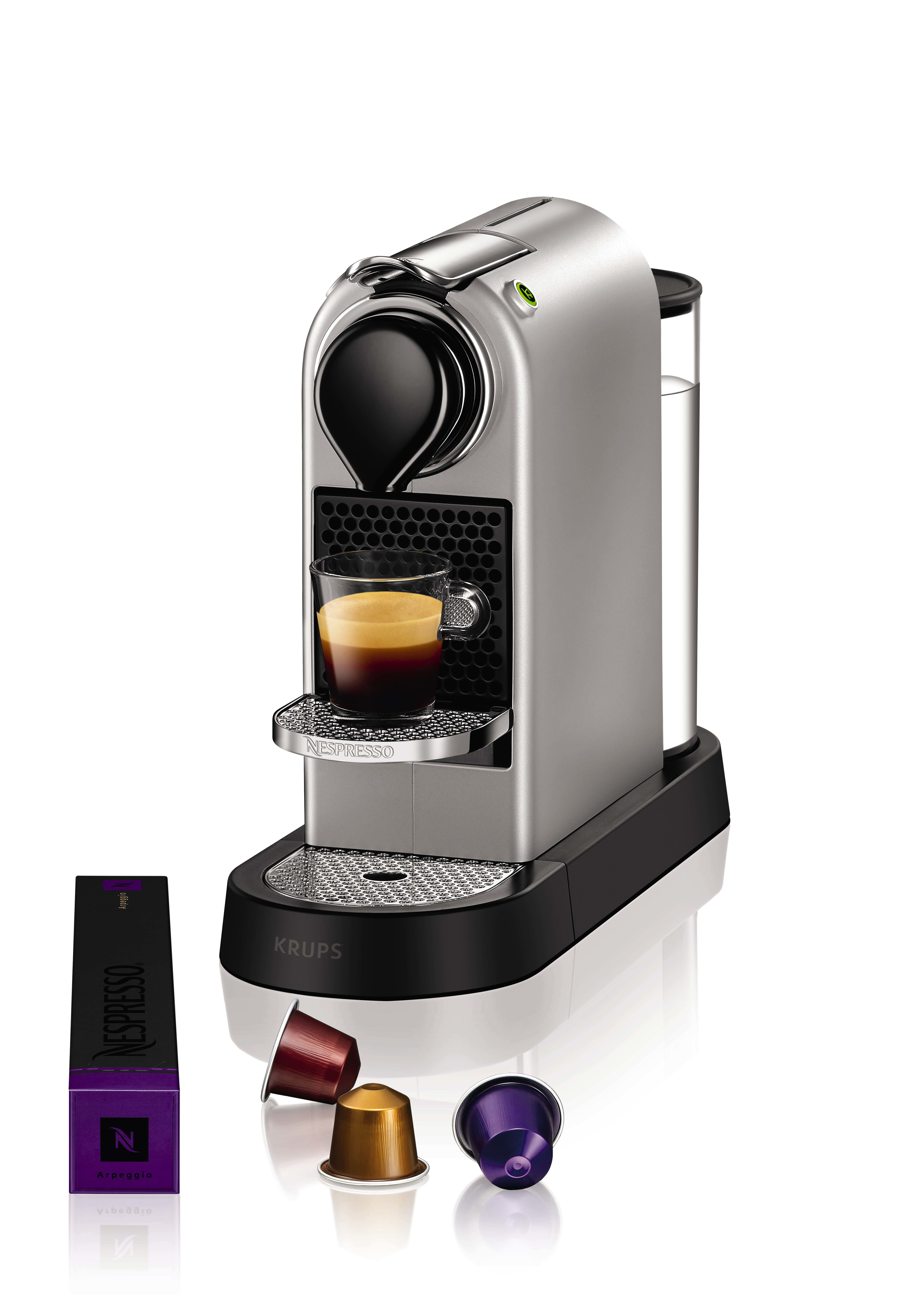 Macchina da caffè Nespresso argentata con bicchiere di caffè. Capsule e scatola visibili. Sfondo bianco.