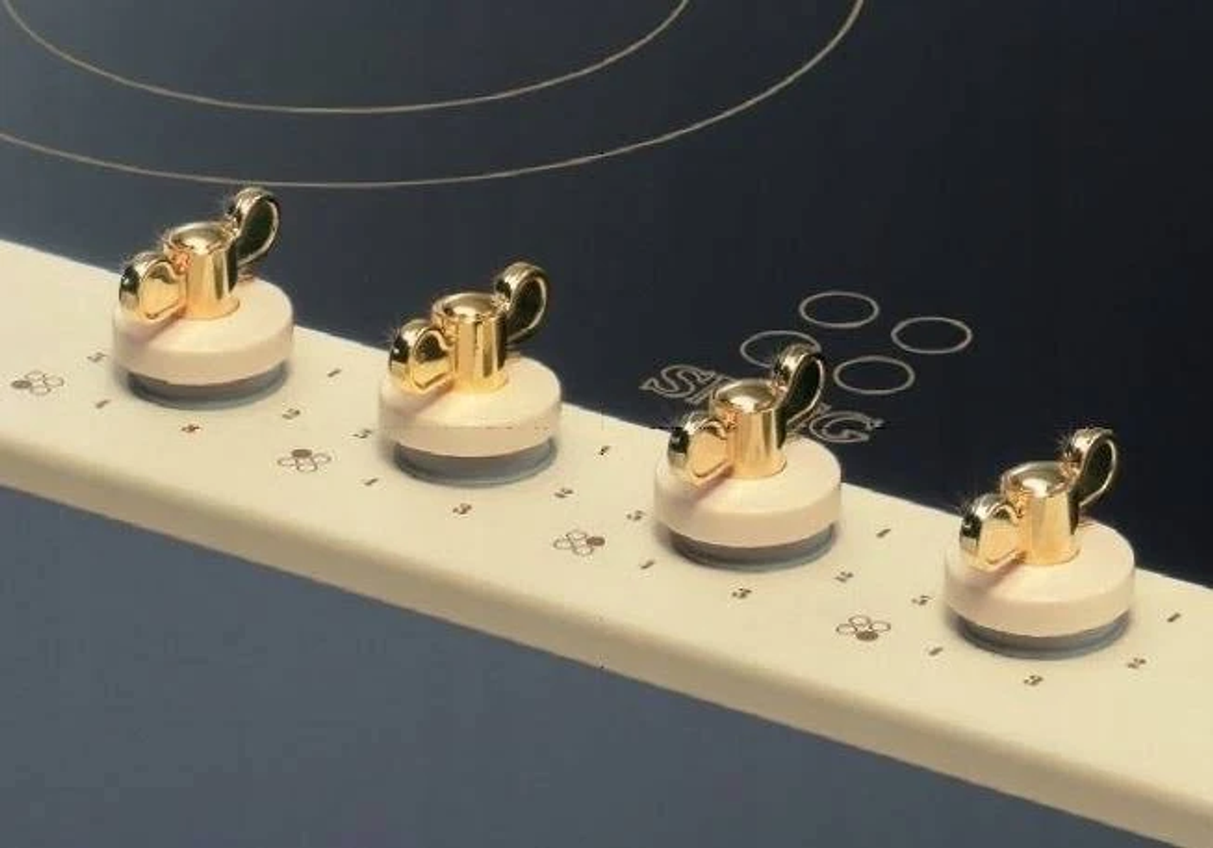 Primer plano de cuatro perillas de control doradas y rosas sobre una superficie oscura.